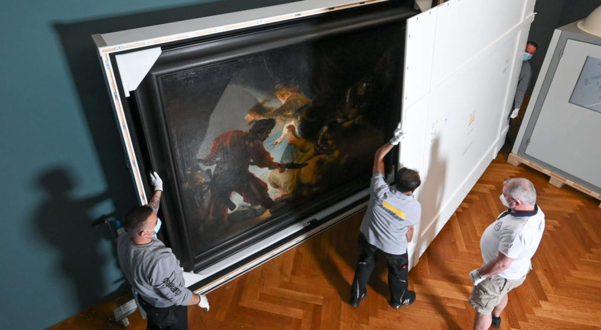 Downward shot of four men moving a large oil painting that has been boxed up
