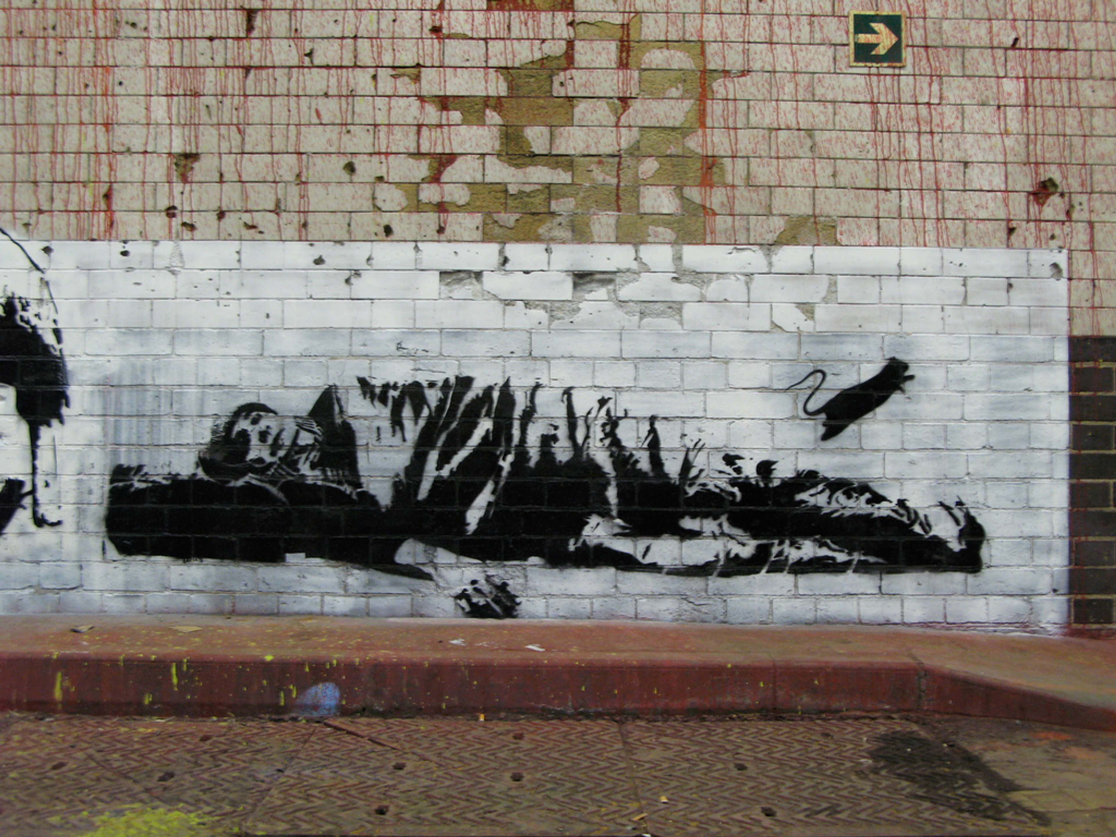 Street art of a figure sleeping rough as a rat jumps away from his body