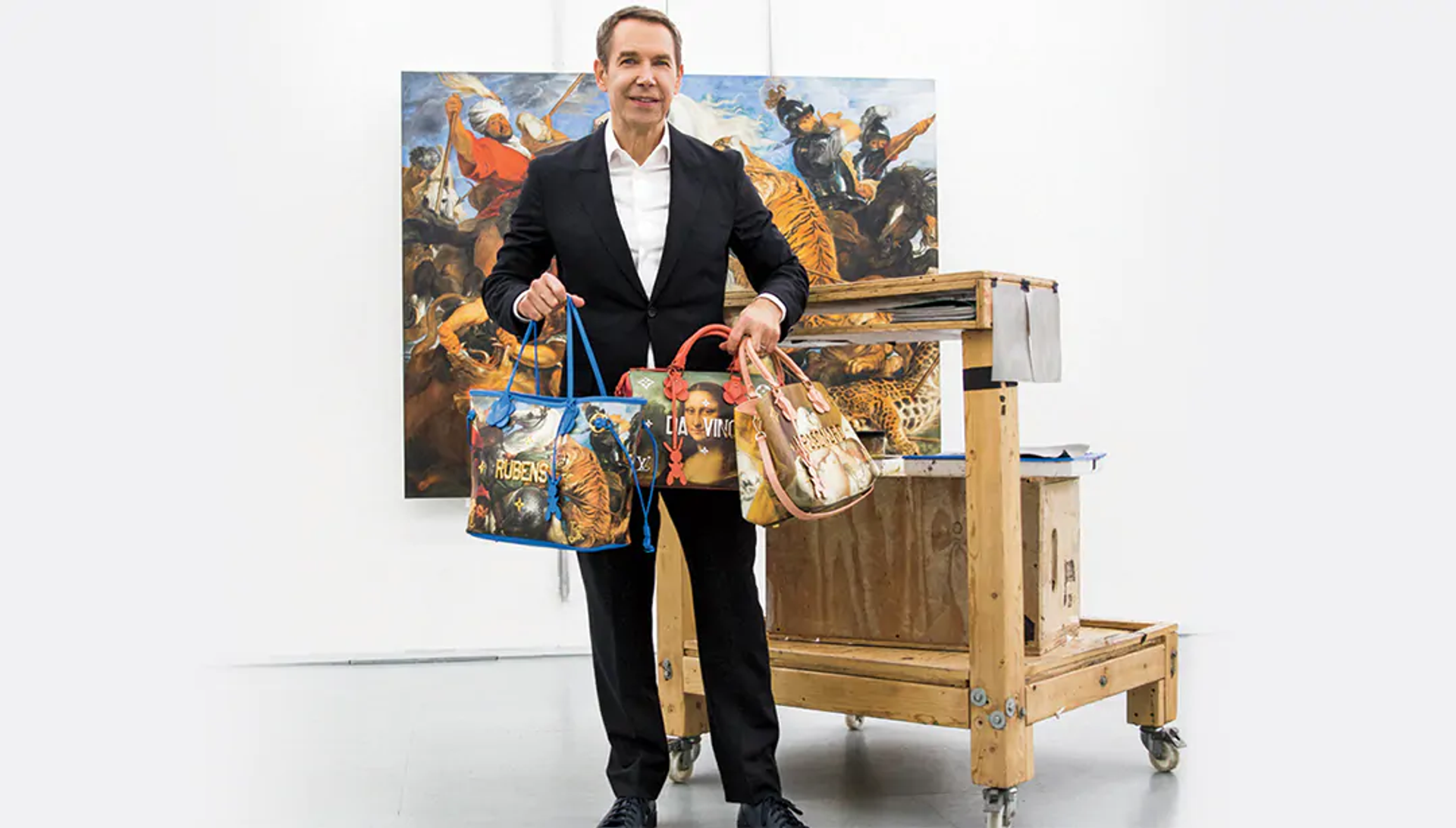 Image of Jeff Koons stood in front of a Renaissance painting, holding three bags from his Masters collection with Louis Vuitton