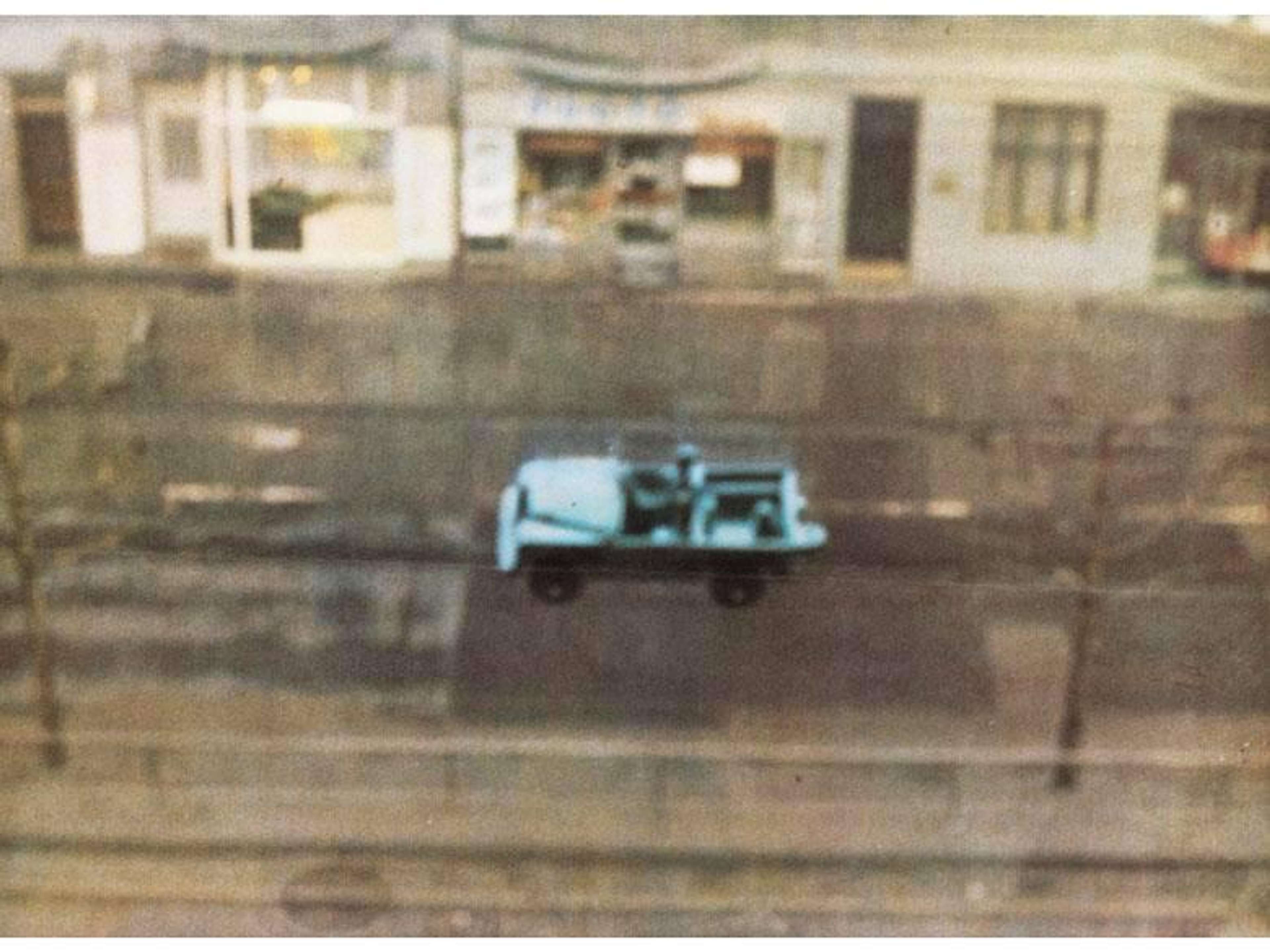 Blurry lithograph by Gerhard Richter, depicting a light blue car on the road. The Street is depicted in muted brown and beige tones.