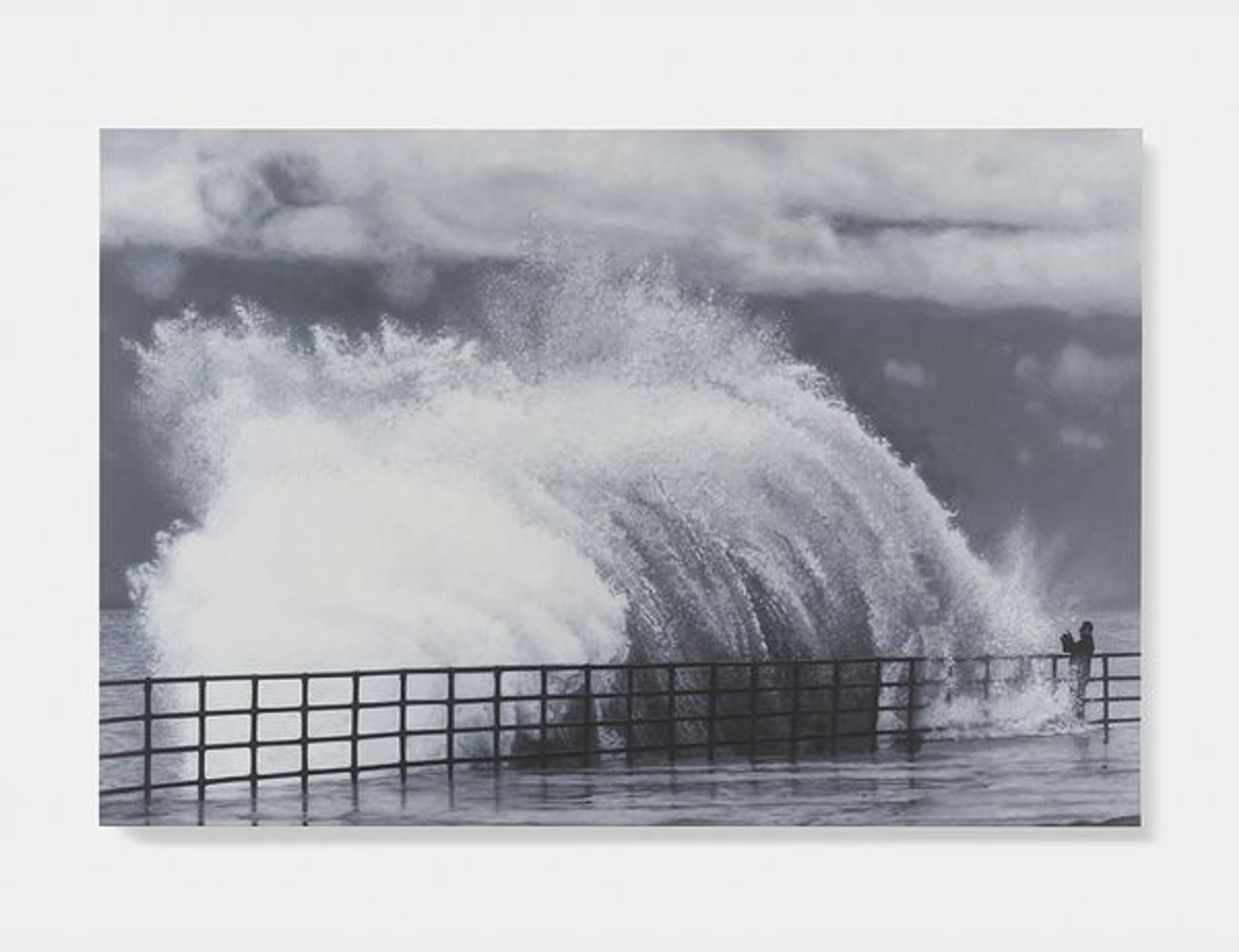 An image of the painting Whitecap by Damien Hirst, showing a large wave overcoming a sea barrier. To the bottom right corner, the figure of a person is hugely outsized by the wave. The painting is done in greyscale.