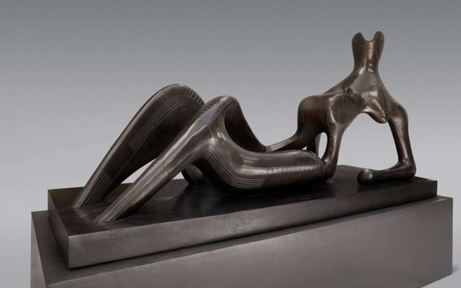 A bronze sculpture depicting an abstract reclining figure on a pedestal, with bent knees and resting on the forearms.