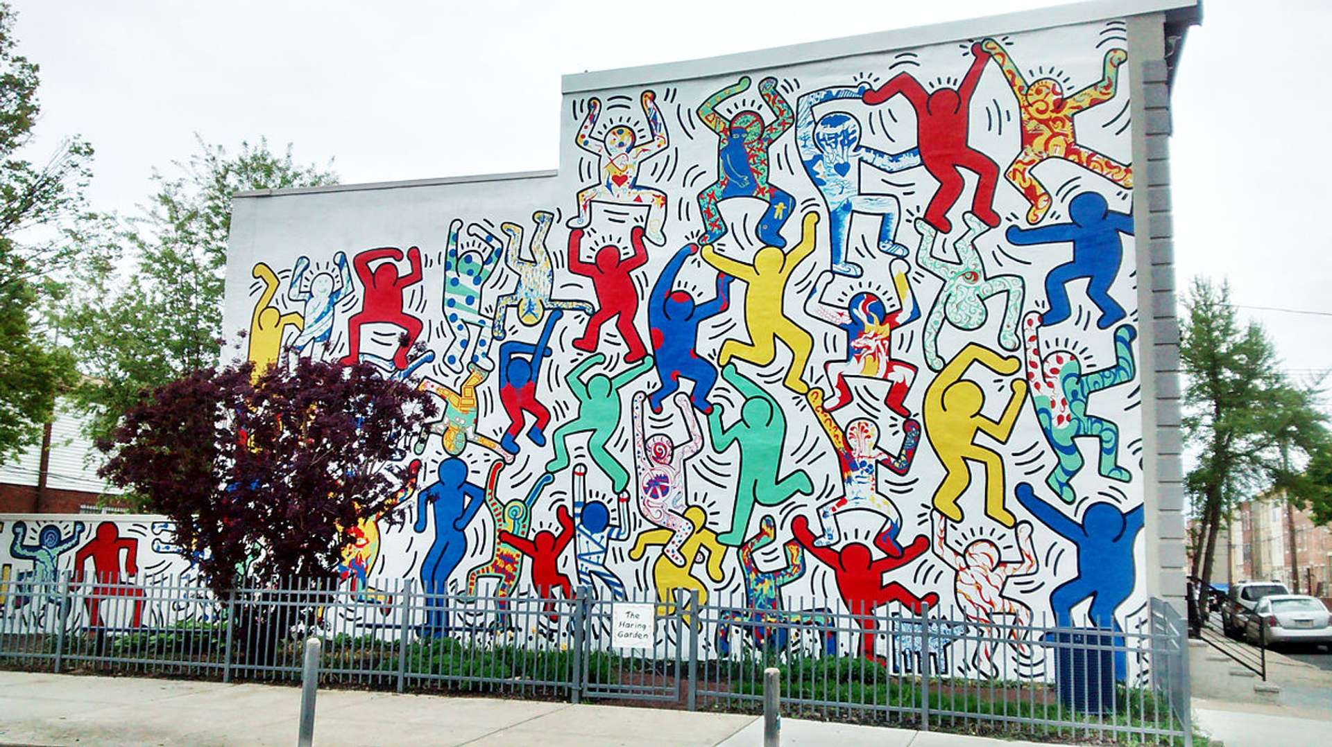 A photograph of Keith Haring's mural "We Are The Youth" at 22nd and Ellsworth Streets in Philadelphia. The mural depicts many multicoloured figures.