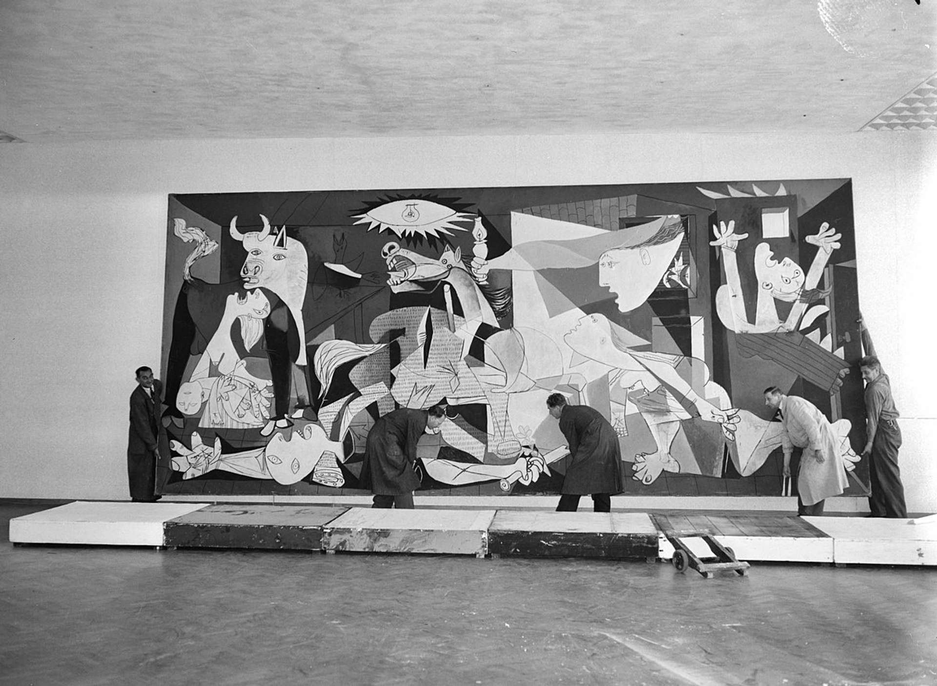 A black and white photograph of Pablo Picasso's 1937 painting, Guernica, being installed at Stedelijk Museum.