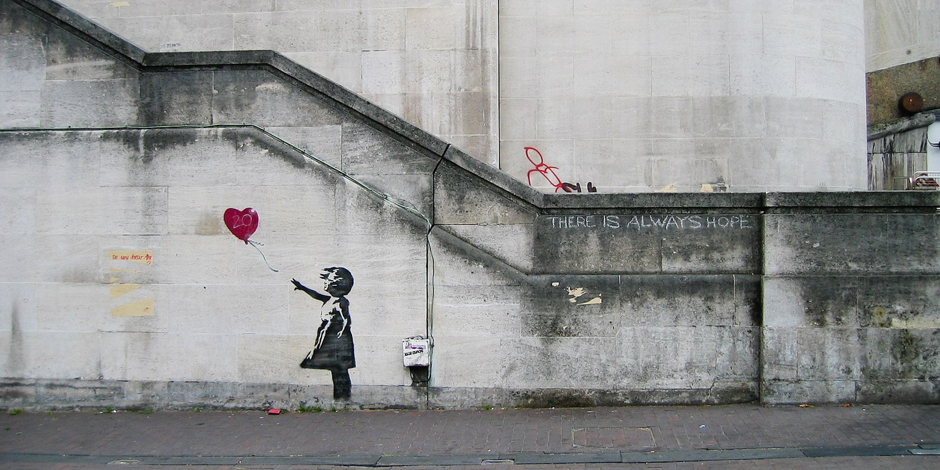 An image of a cityscape with the Girl With Balloon artwork by Banksy, depicting a young girl reaching out for a red, heart shaped balloon.