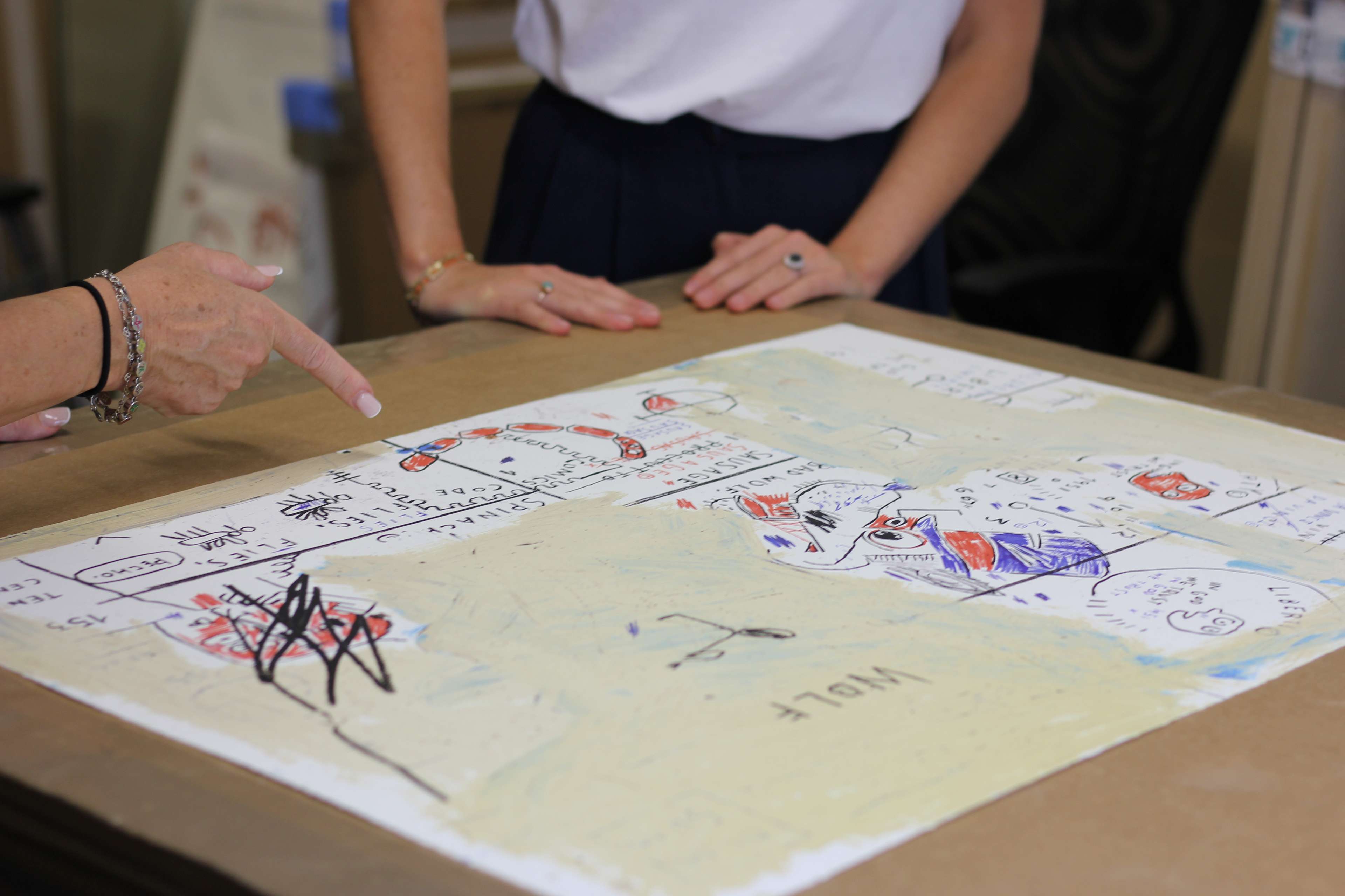 Two people standing next to an artwork on a table, with one pointing to it.