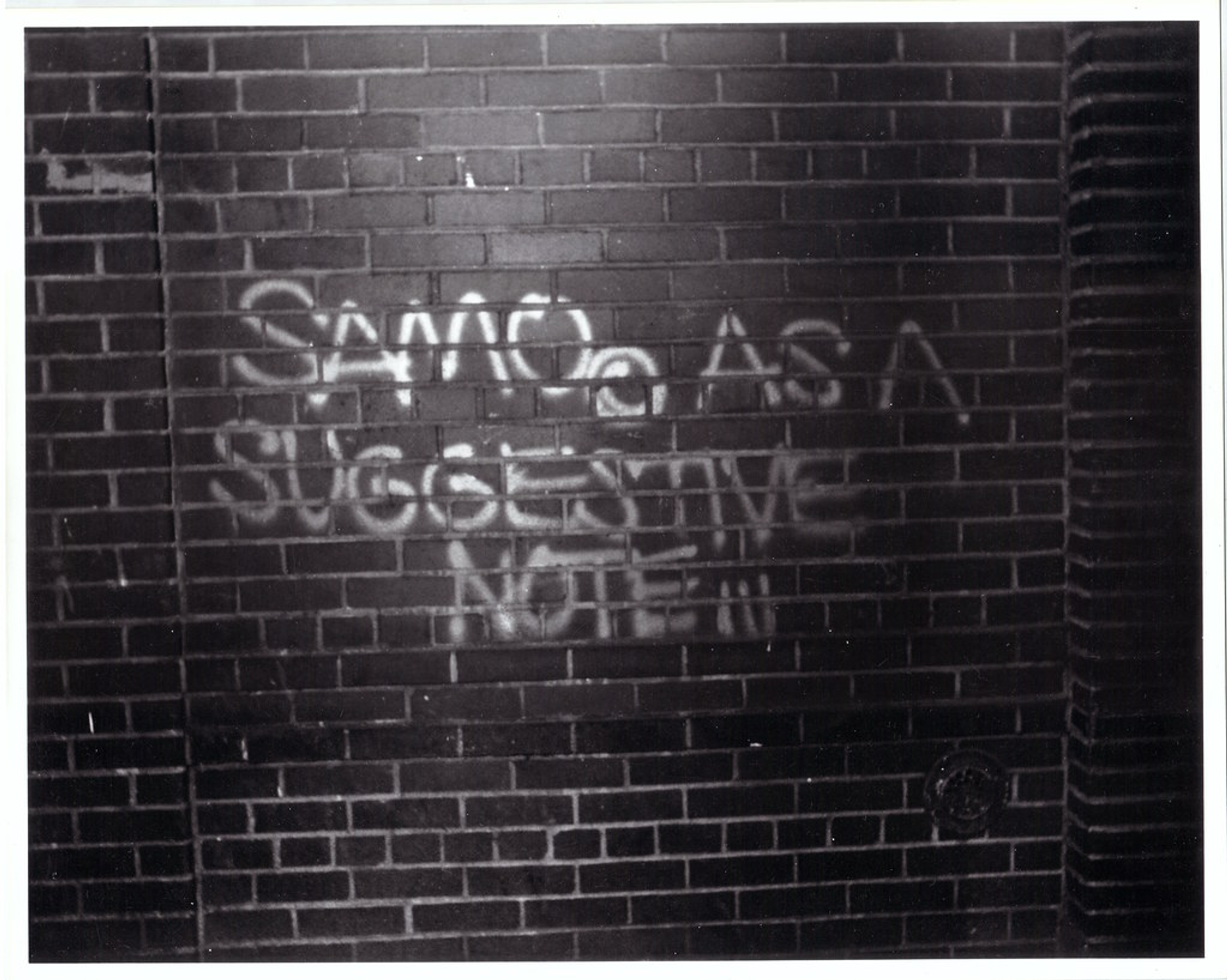 An image of graffiti by SAMO on a brick all. It reads "SAMO AS A SUGGESTIVE NOTE."