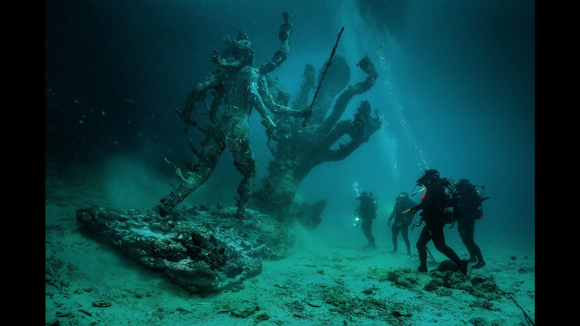 This image shows a group of divers underwater, looking at two giant statues.