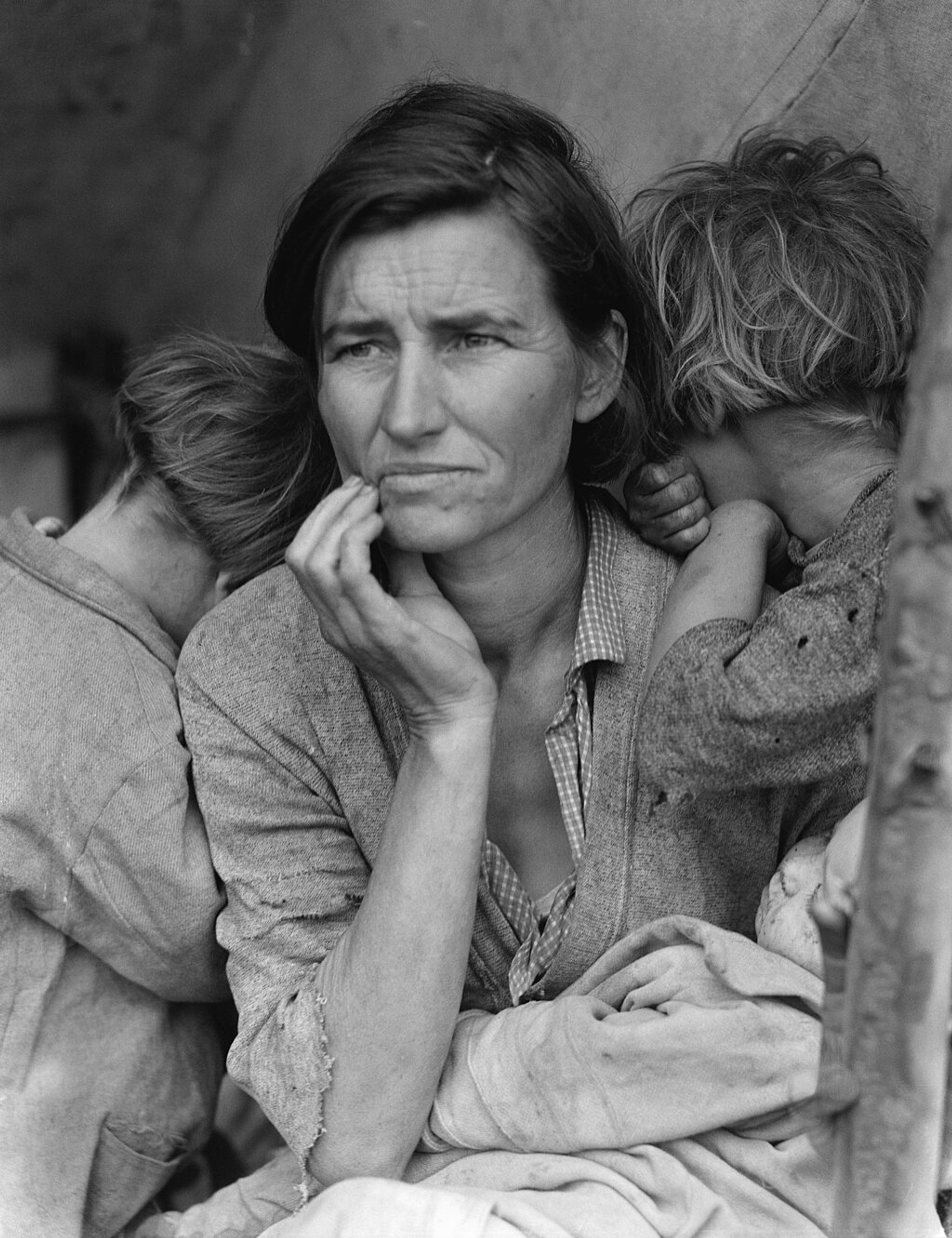 A black and white photograph of a woman with her two children. She has a despondent and worried look on her face.