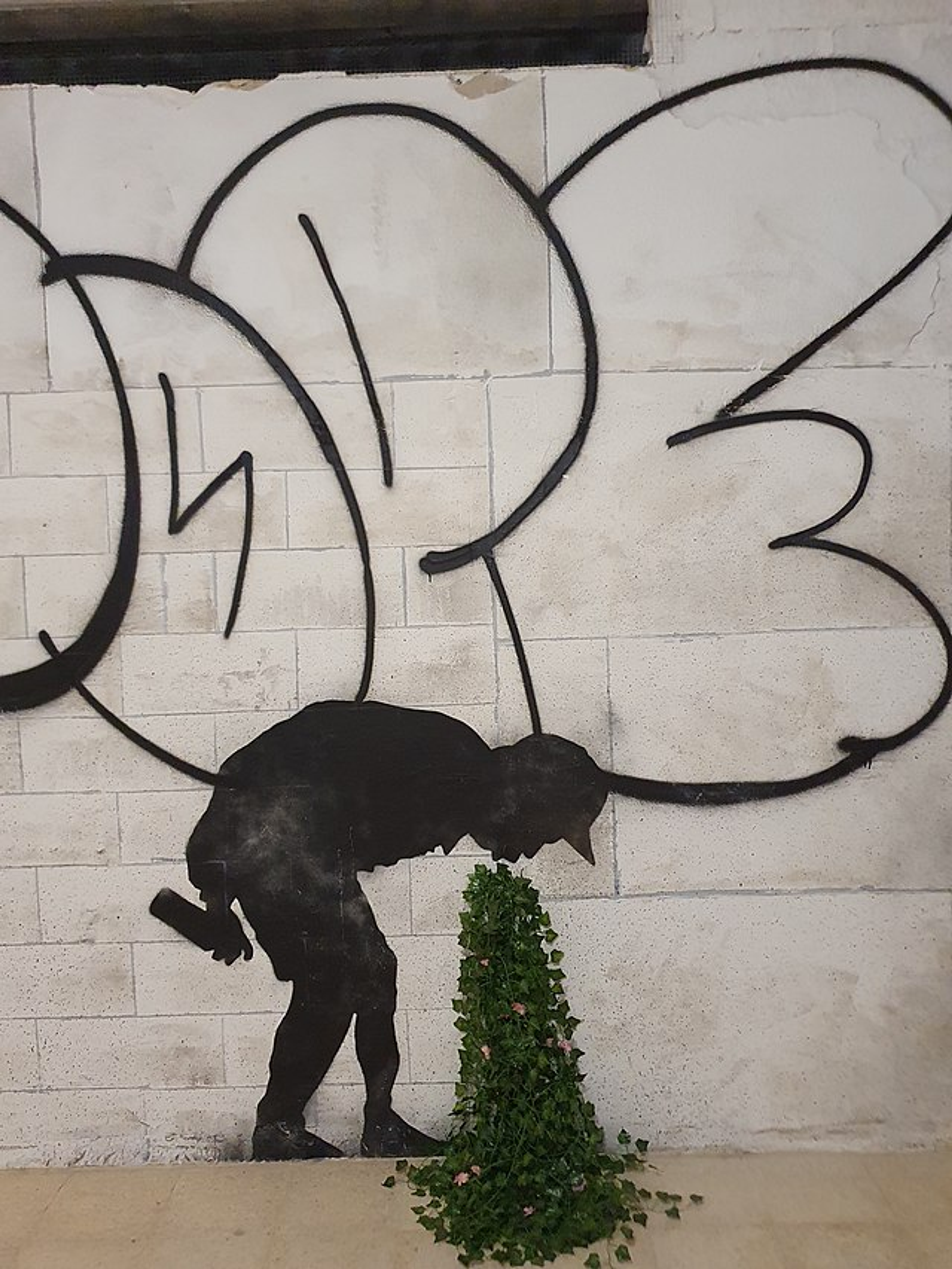 Ce graffiti représente une figure masculine penchée en avant, qui semble vomir un bouquet de feuillage.