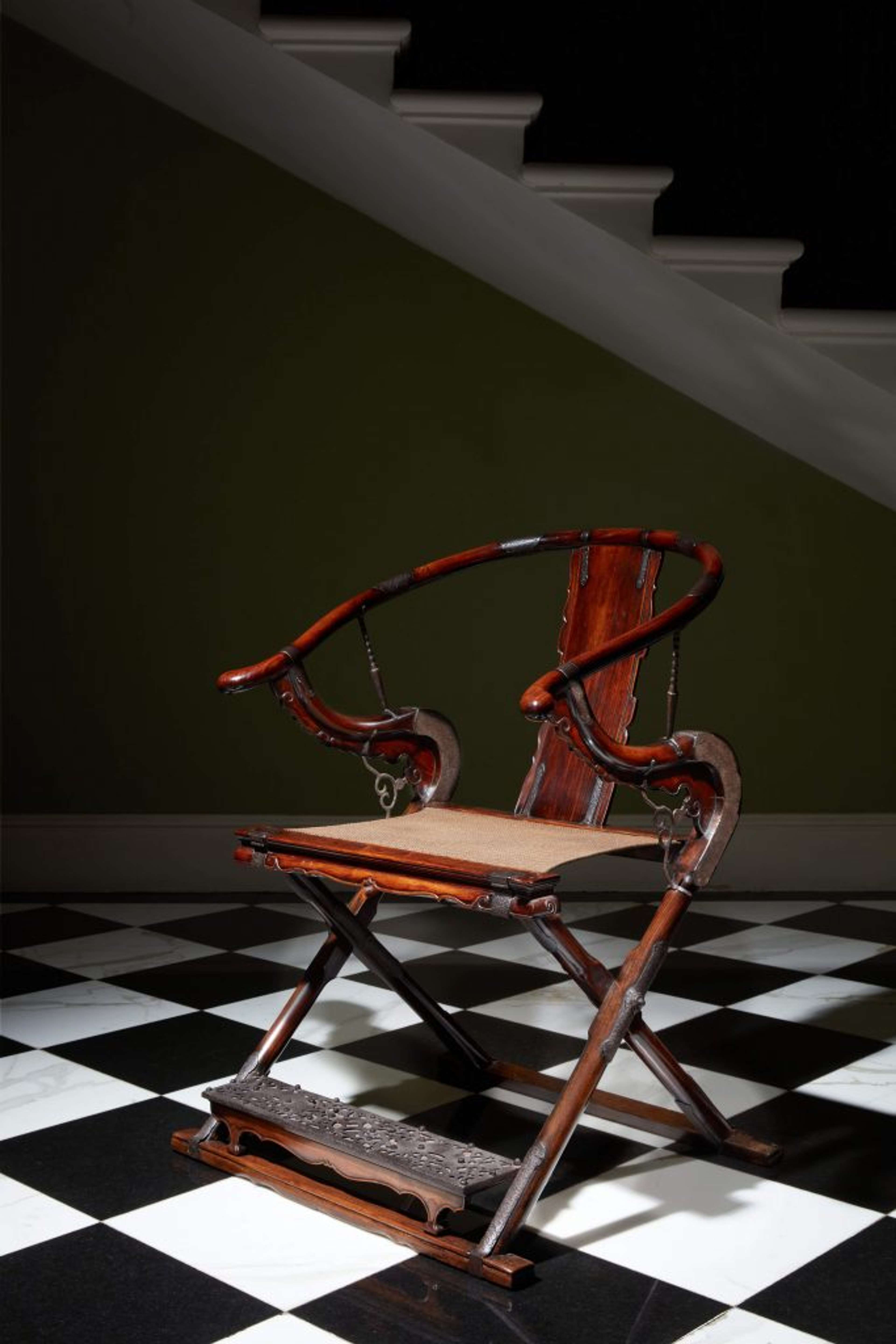 Une chaise décorative en bois avec des courbes et un repose-pieds décoratif, posée sur un sol à damier noir et blanc.