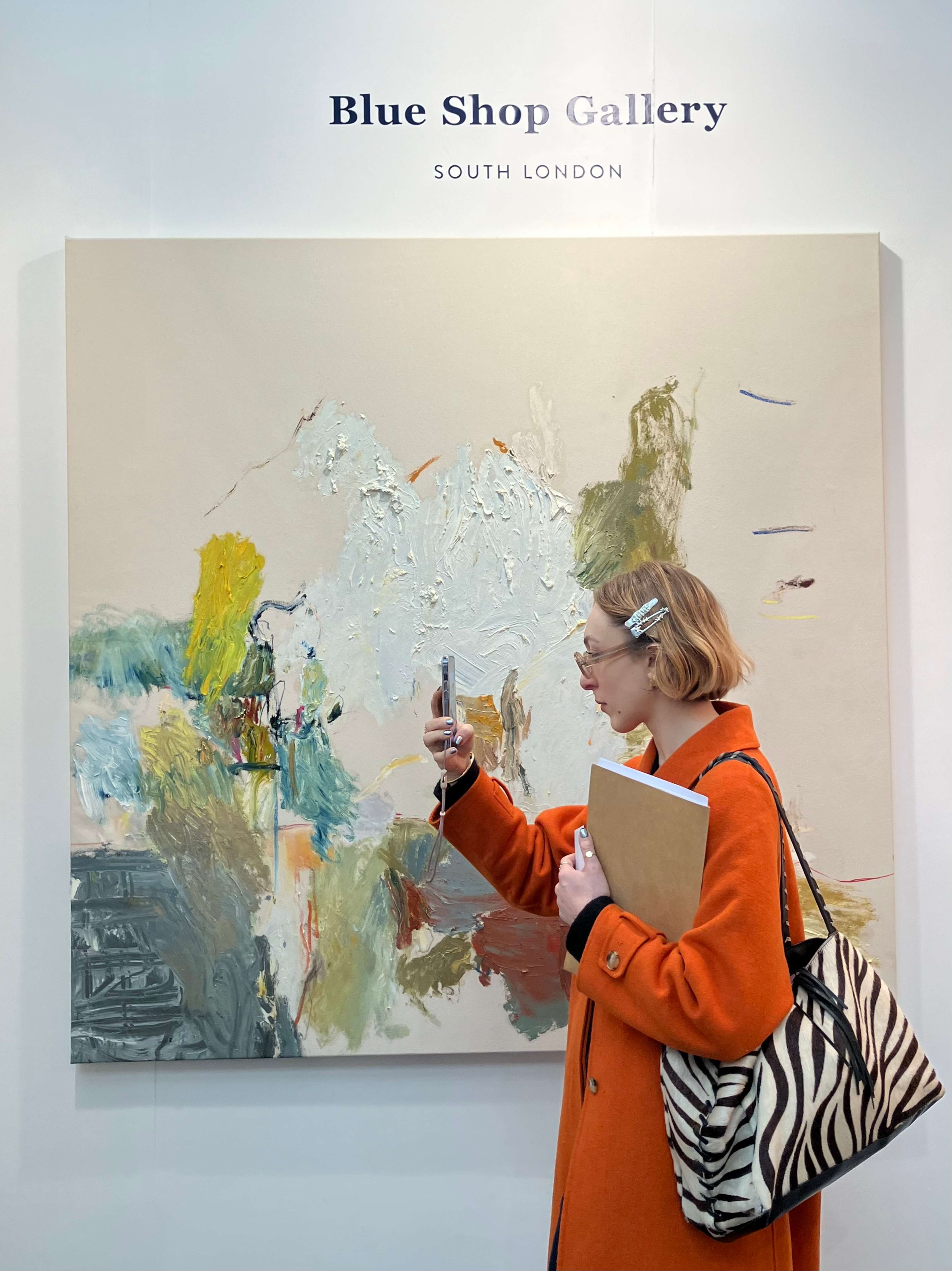 Une jeune femme se tient devant une grande œuvre d'art et prend en photo quelque chose qui est hors champ.