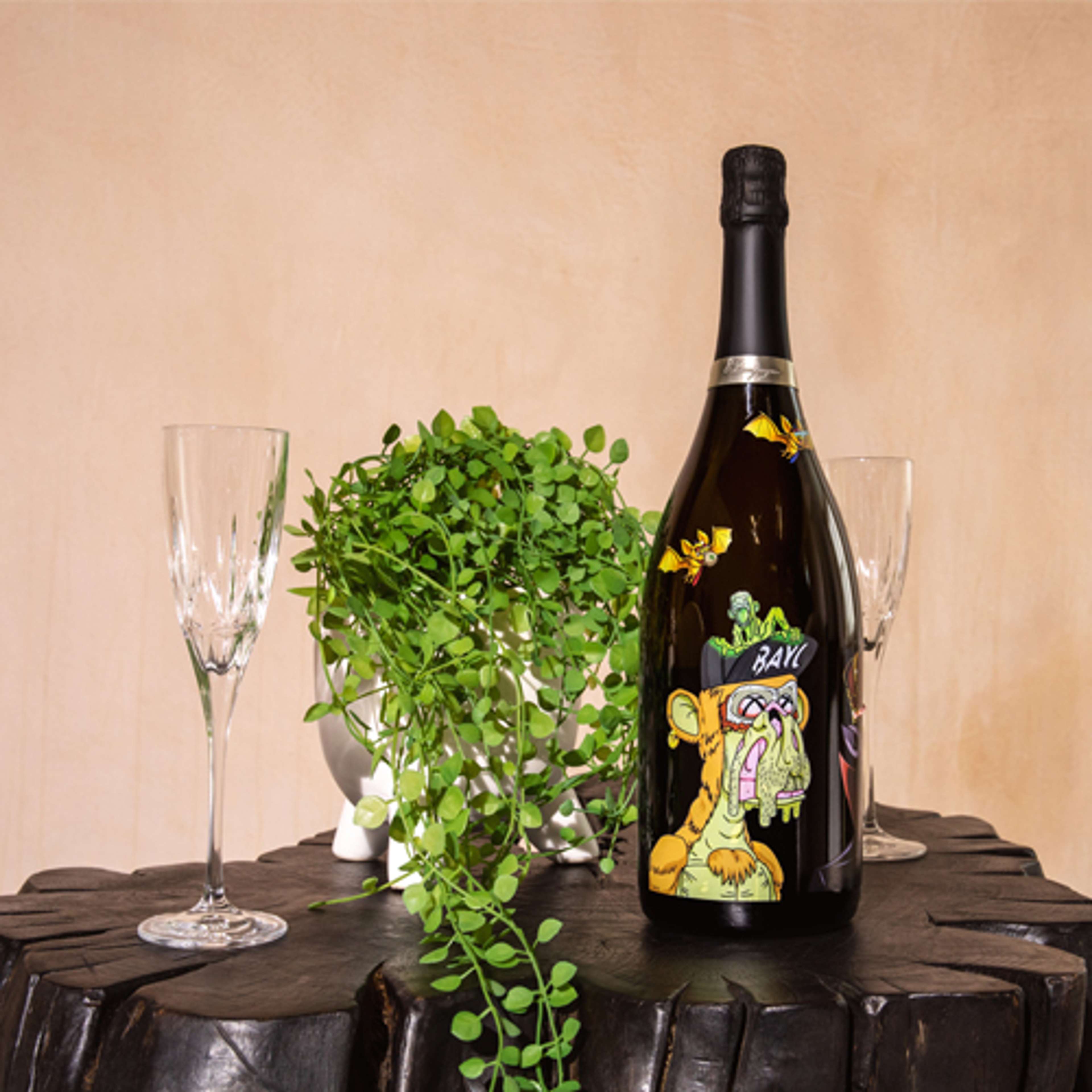 Une bouteille de vin noire ornée d'un graphique de singe jaune, accompagnée de deux verres et d'une plante verte, le tout posé sur une petite table d'appoint en bois noir.