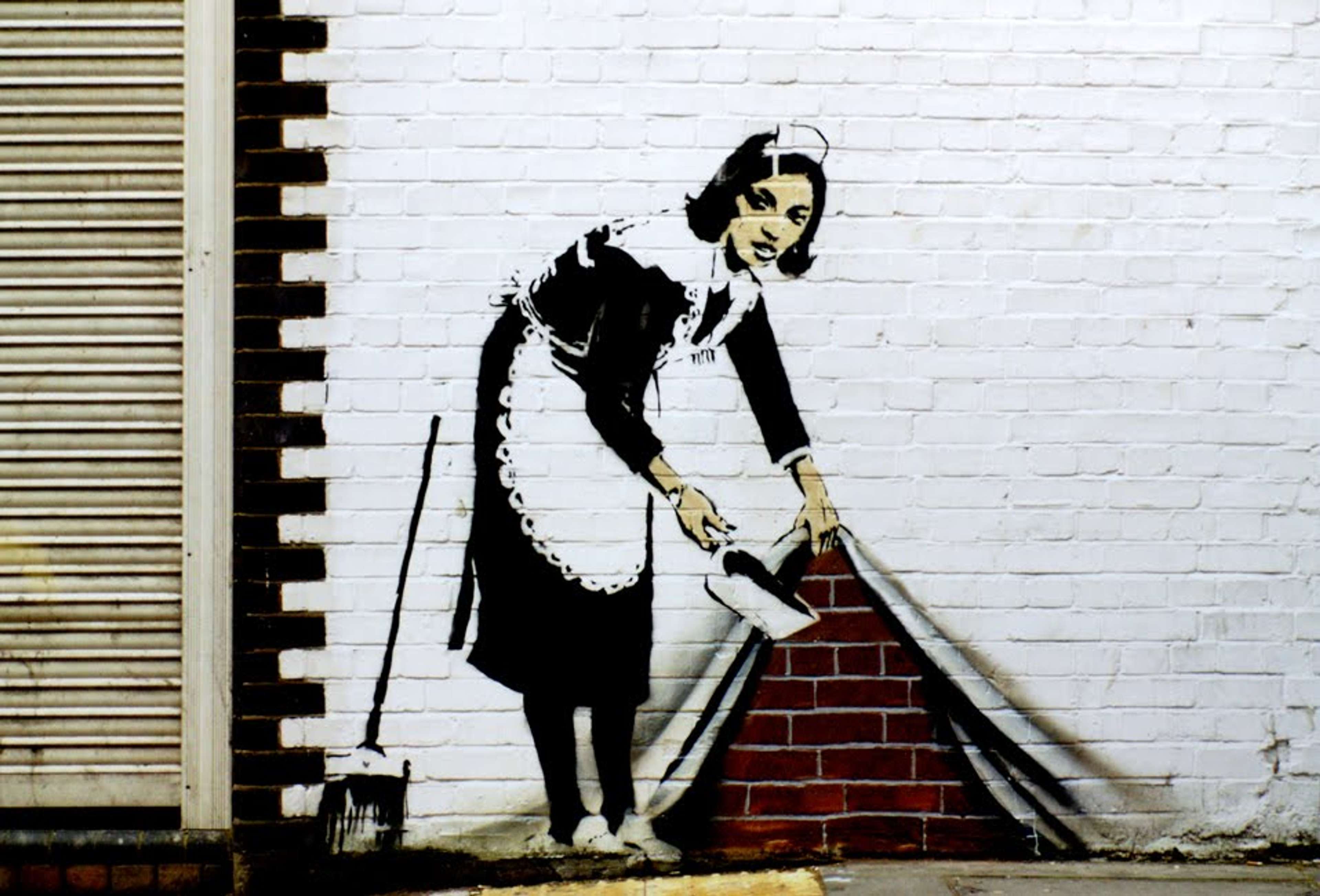 Une fresque de street art de Banksy représentant une femme en uniforme de femme de chambre, semblant soulever un rideau blanc pour révéler le mur de briques dessous où elle jette ses balayures.