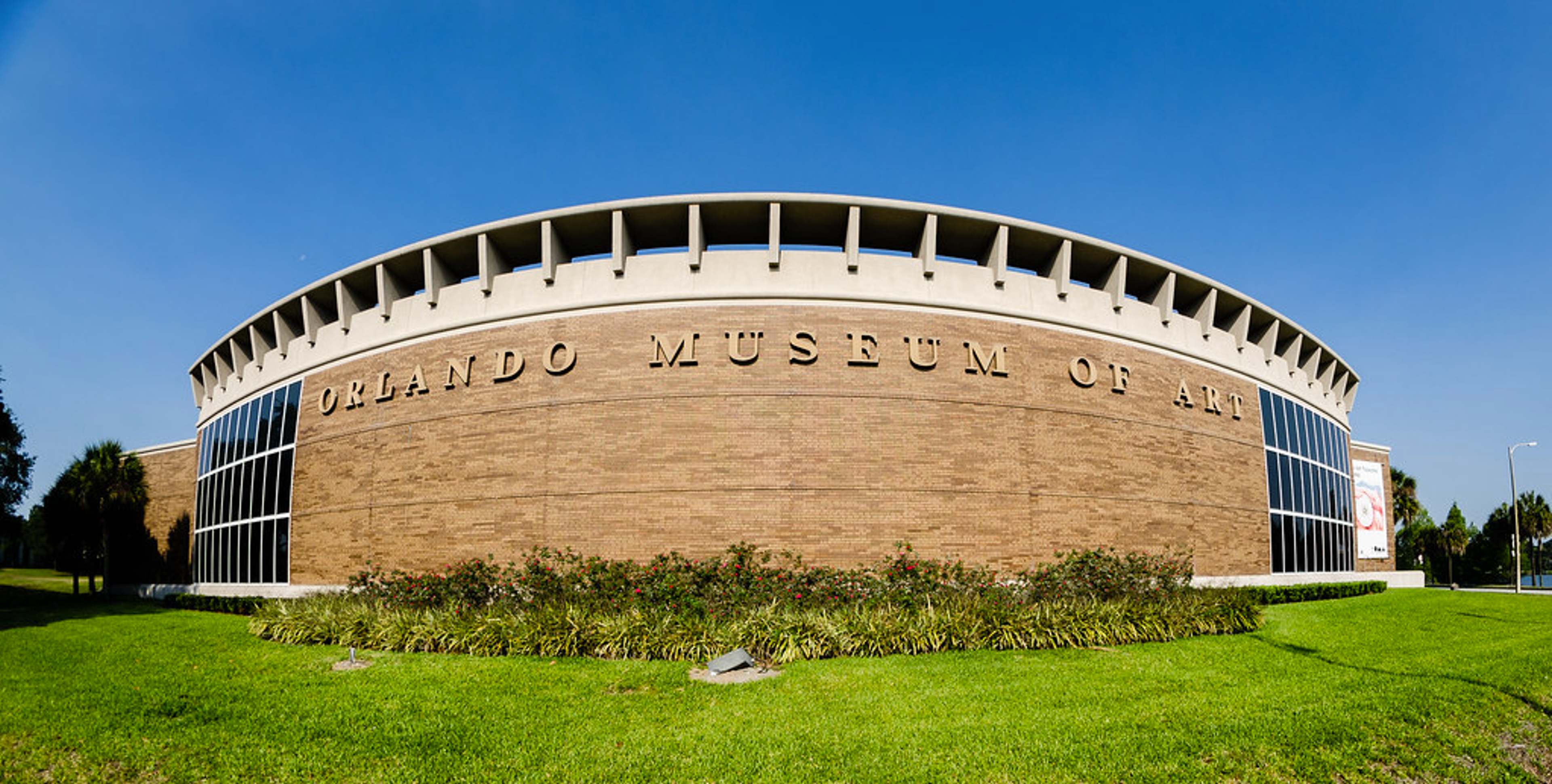 Image extérieure du Orlando Museum of Art. Elle montre un bâtiment circulaire avec des fenêtres de chaque côté, sur fond de ciel bleu.