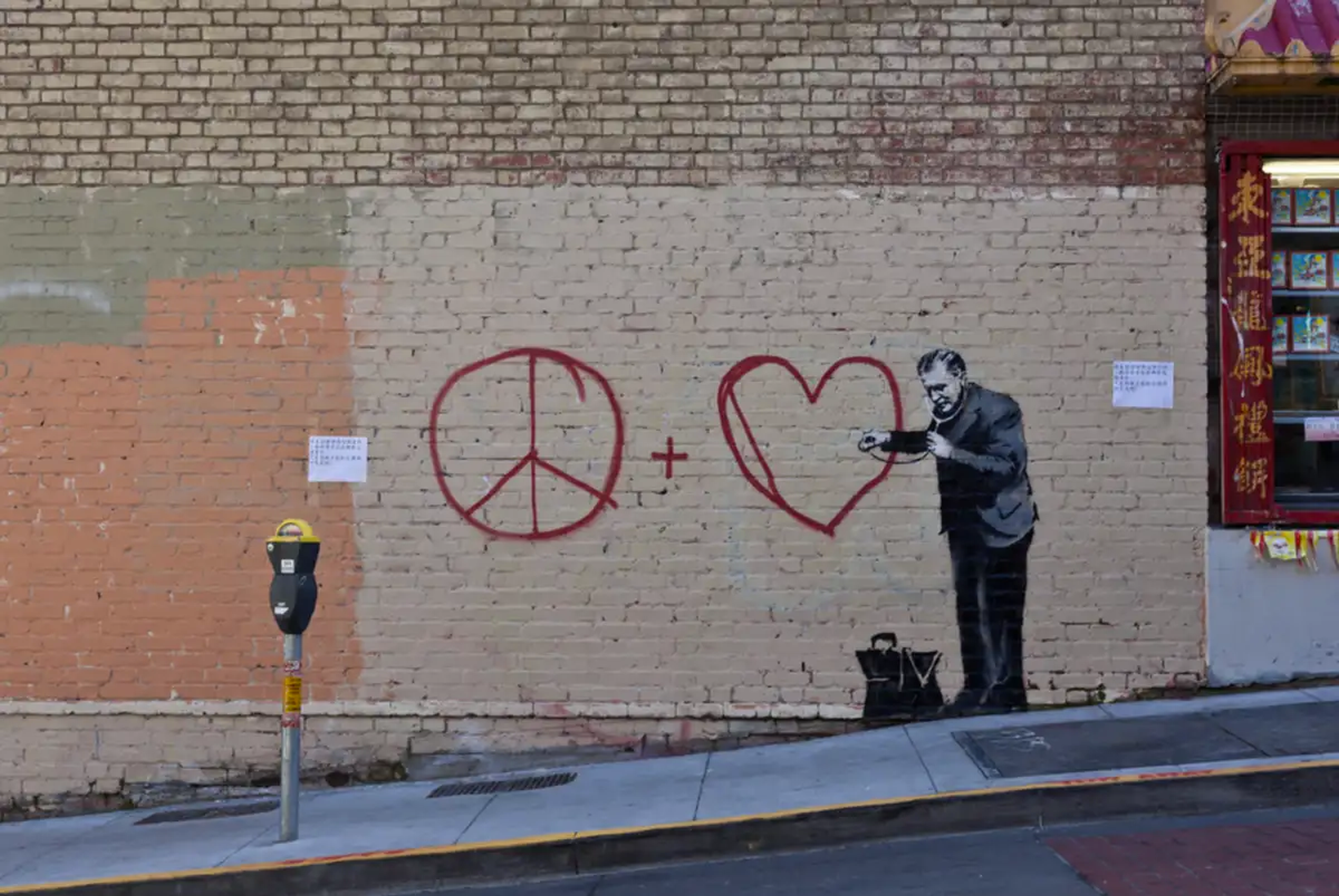Une image de la murale « Peaceful Doctor » de Banksy. Elle représente un homme monochrome, vêtu d'une tenue de médecin, qui écoute le chagrin d'un graffiti simplifié représentant un signe de paix et de « Love Love ».