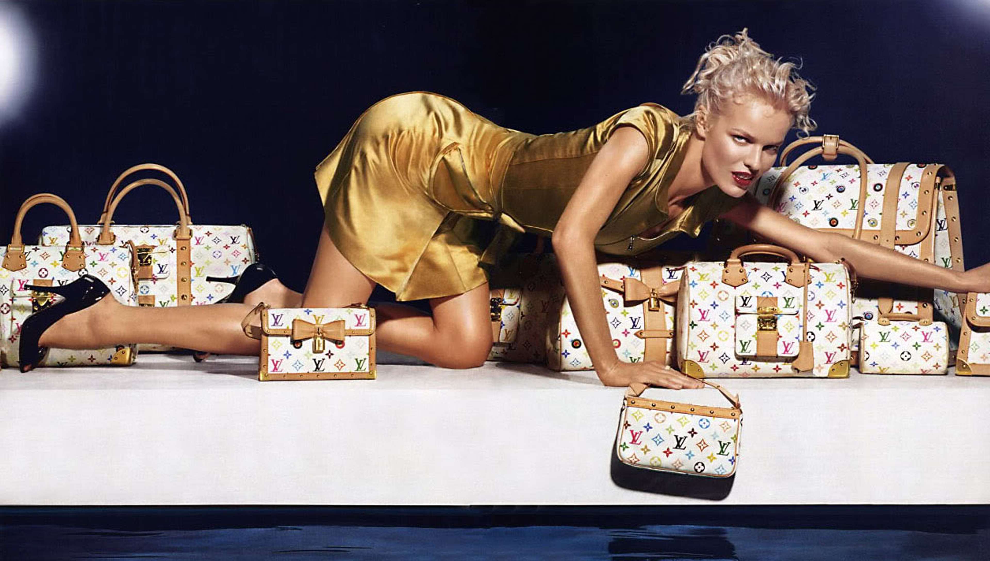 Une image d'un mannequin accroupi au-dessus d'un grand nombre de sacs et de bagages Louis Vuitton, réinterprétés dans la palette colorée de Murakami.