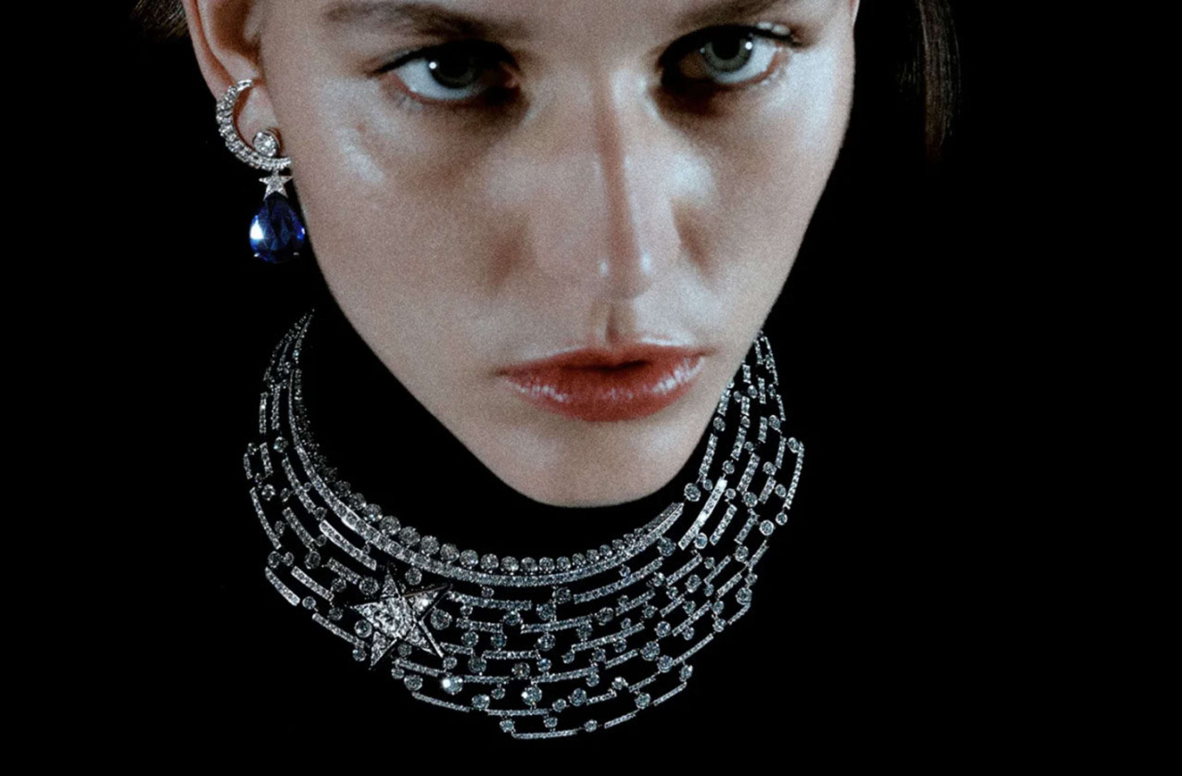 Femme portant un épais collier ras-du-cou argenté composé de maillons, orné d'une étoile sertie de pierres d'un côté, et de boucles d'oreilles en forme de lune et d'une pierre bleue suspendue à une étoile reliée.