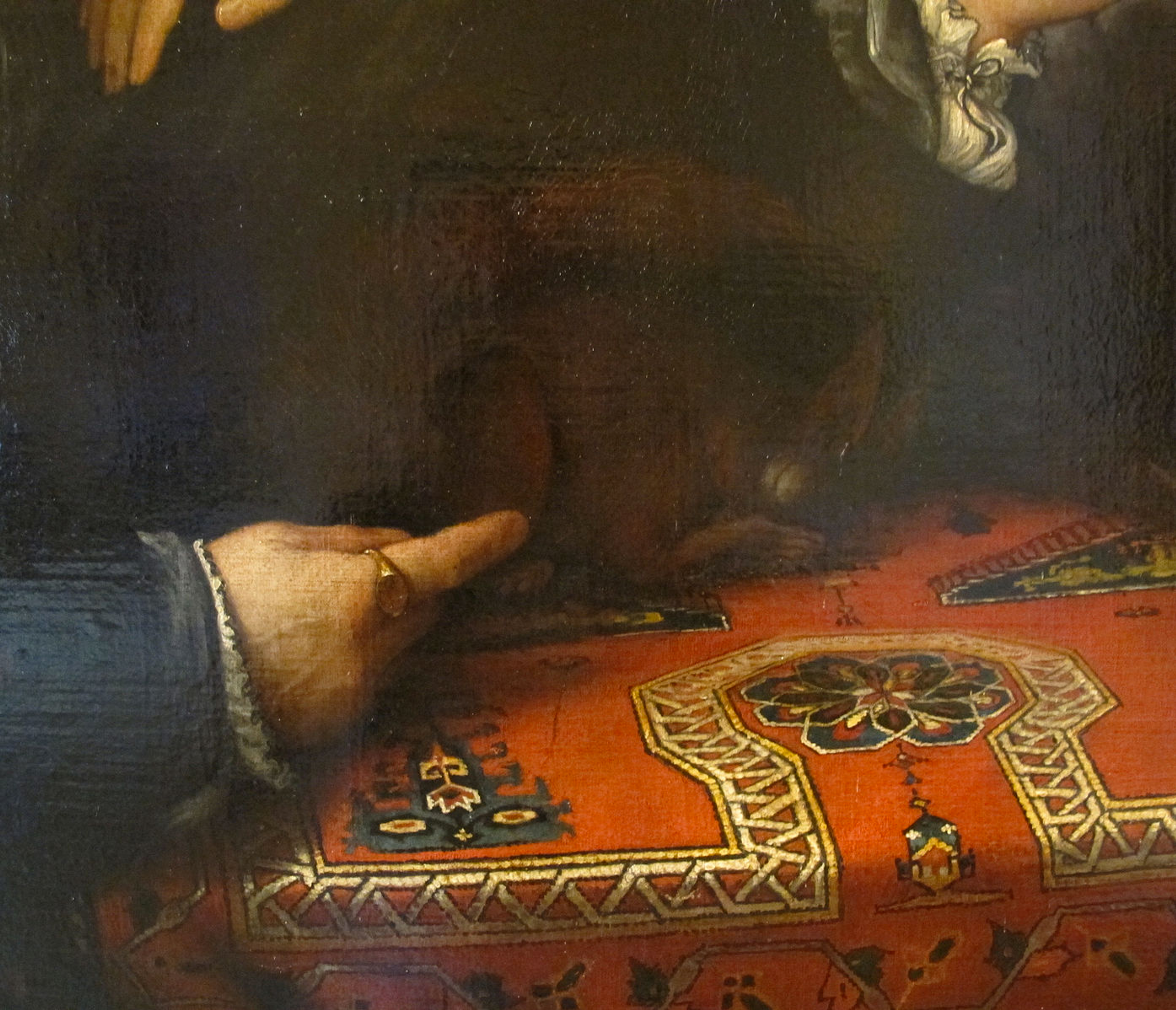 Gros plan sur une œuvre de la Renaissance de Lorenzo Lotto. Elle représente la main d'un homme reposant sur une nappe au motif audacieux.