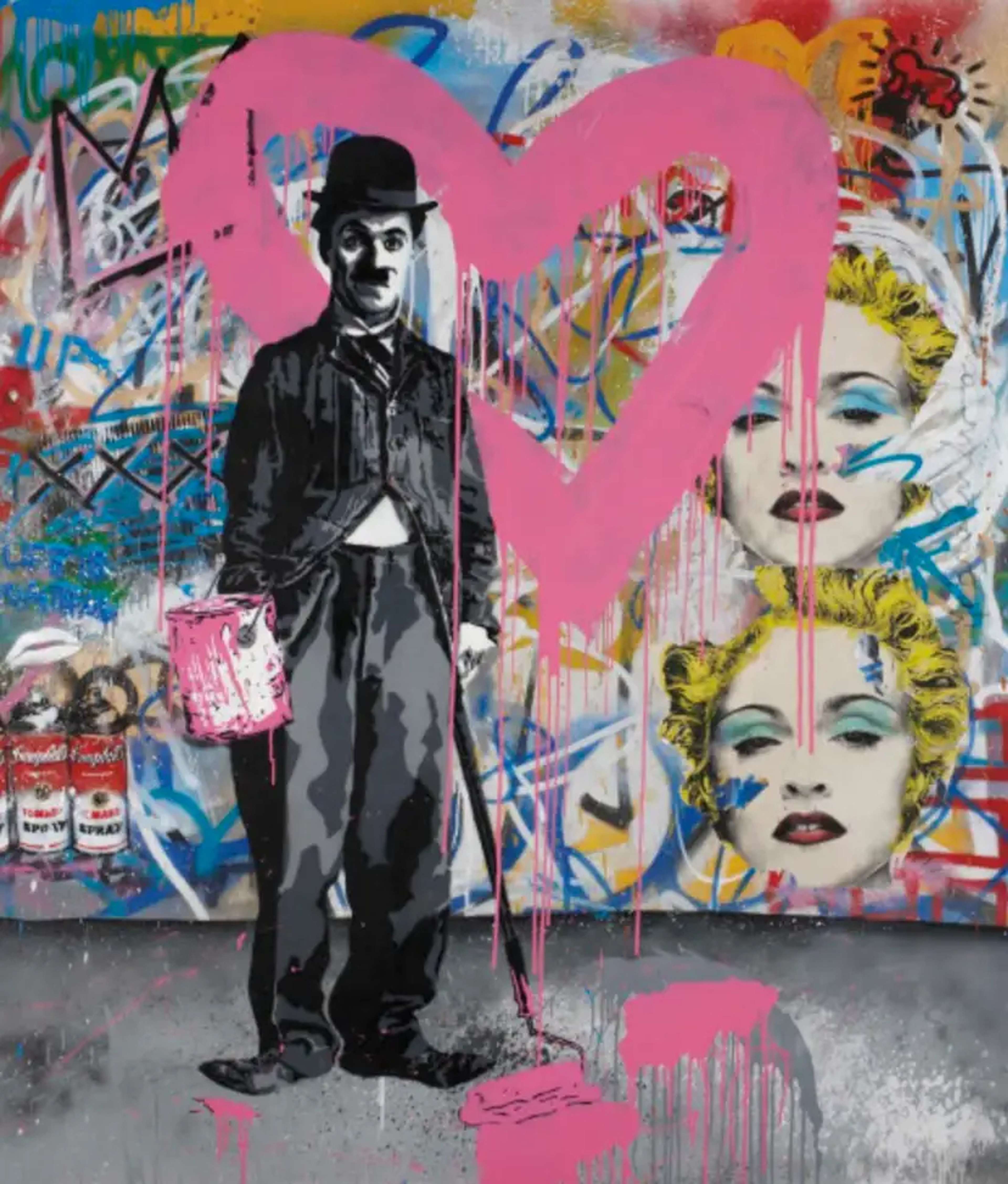 Une œuvre d'art de style graffiti représentant un portrait pochoir de la célébrité Charlie Chaplin, tenant une boîte de peinture rose ouverte. L'œuvre est placée sur un mur couvert de graffitis, orné de portraits pochoir de Madonna et d'un contour de cœur rose bien visible. L'œuvre s'intitule « The Cat And The Heart - Pink ».