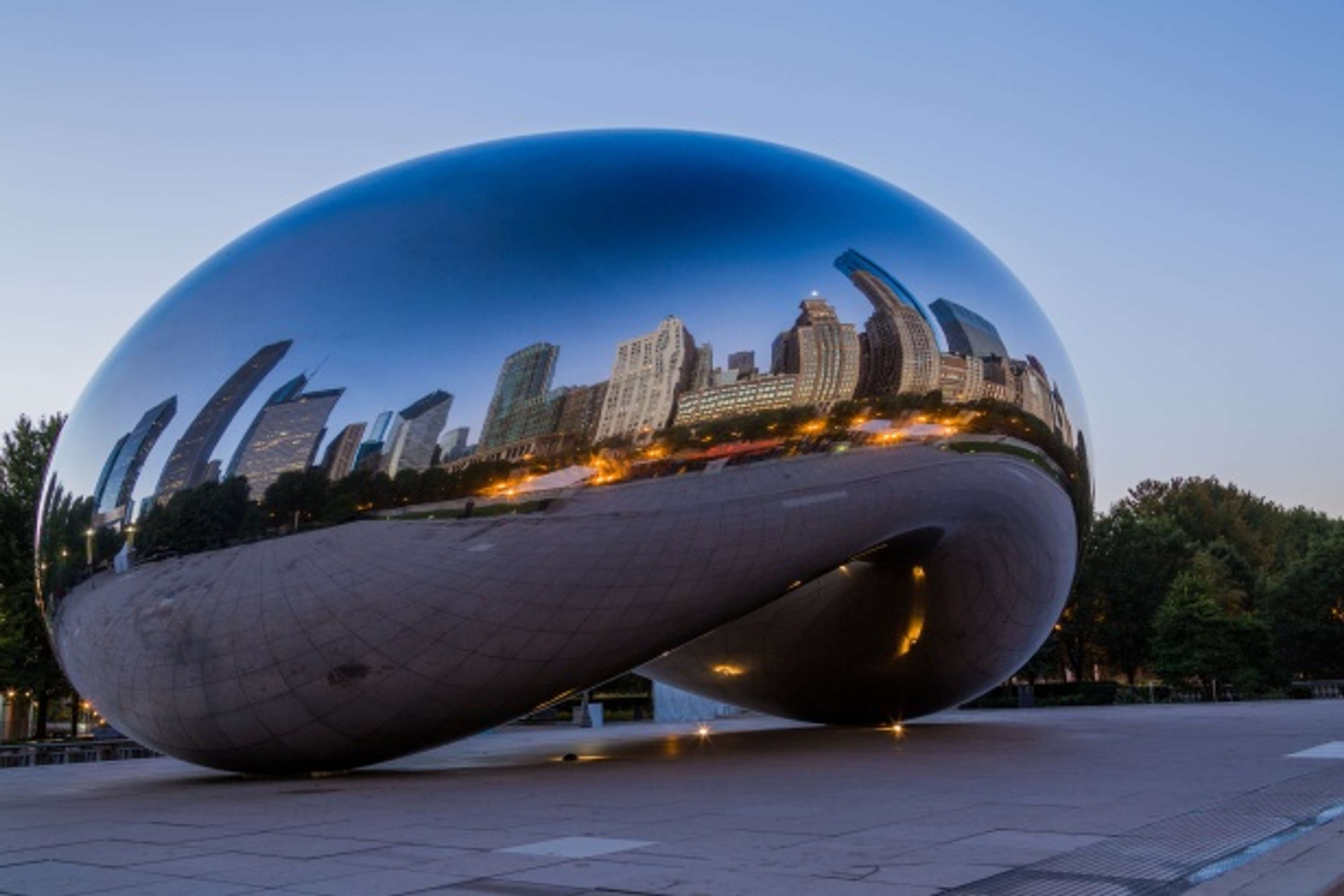 Une image de l'œuvre « Cloud Gate » d'Anish Kapoor. Il s'agit d'une sculpture géante et réfléchissante en forme de haricot, ce qui lui vaut son surnom. On peut voir le paysage urbain de Chicago se refléter dans l'œuvre.