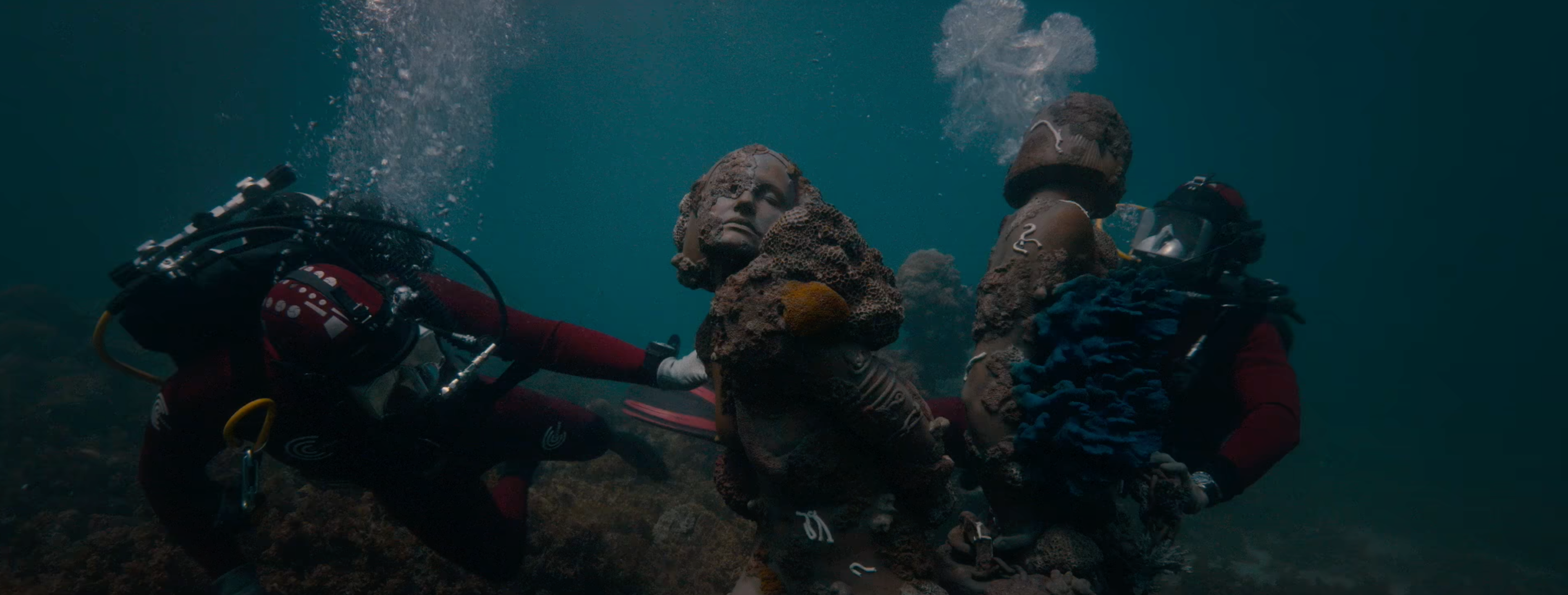 Cette image montre deux plongeurs sous l'eau, manipulant deux statues.