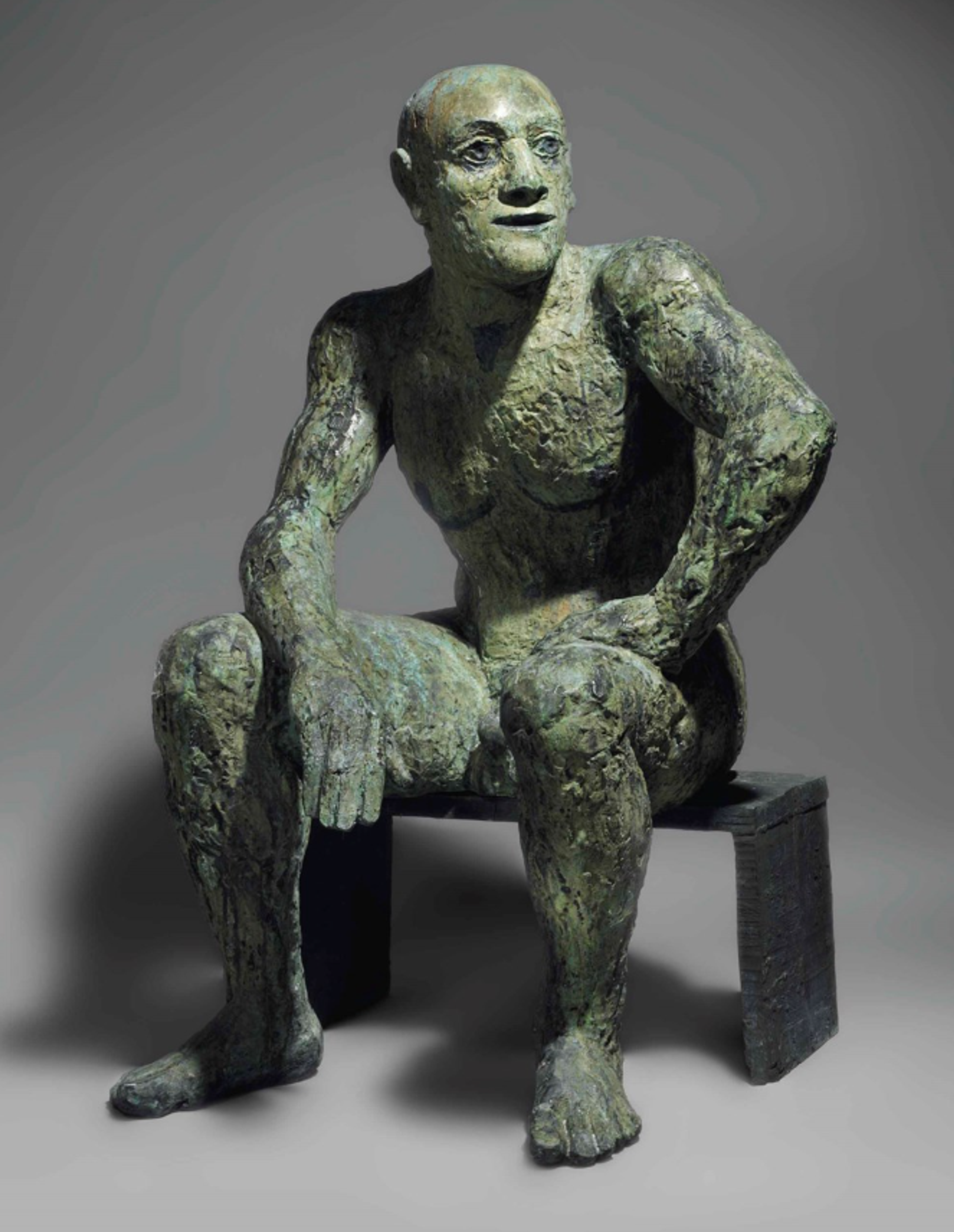 A textured bronze sculpture of a man seated on a simple geometric bench. He looks off to the left, with his left hand propped up on his left thigh. His right arm hangs relaxed between his legs, his elbow connected with his knee.