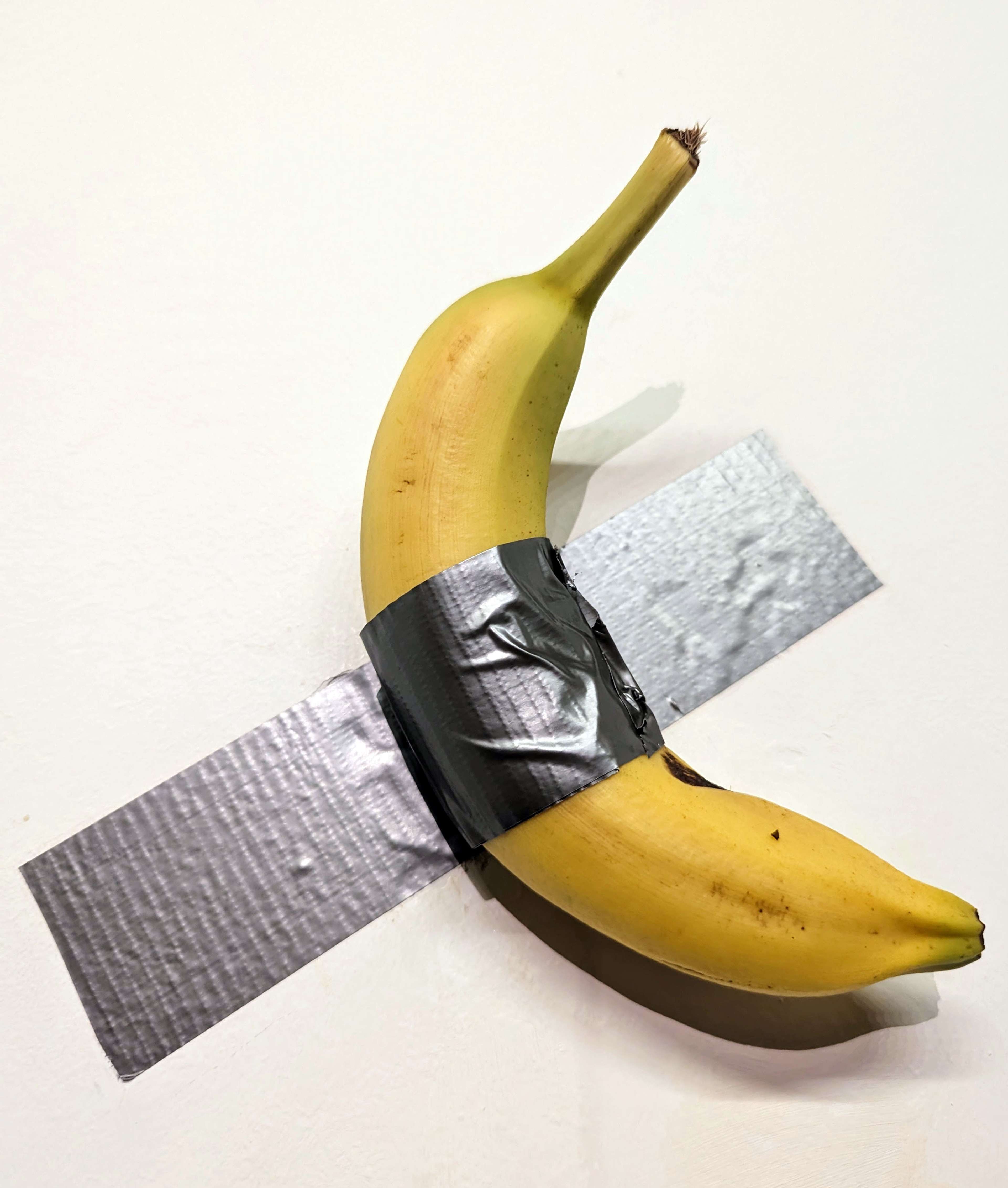 Une banane jaune mûre scotchée à un mur blanc de galerie dans un style minimaliste. L'absurdité de cet objet du quotidien présenté comme une œuvre d'art renvoie aux thèmes du conceptualisme et de la marchandisation dans l'art contemporain, faisant écho à la célèbre pièce de Maurizio Cattelan, « Comedian ».
