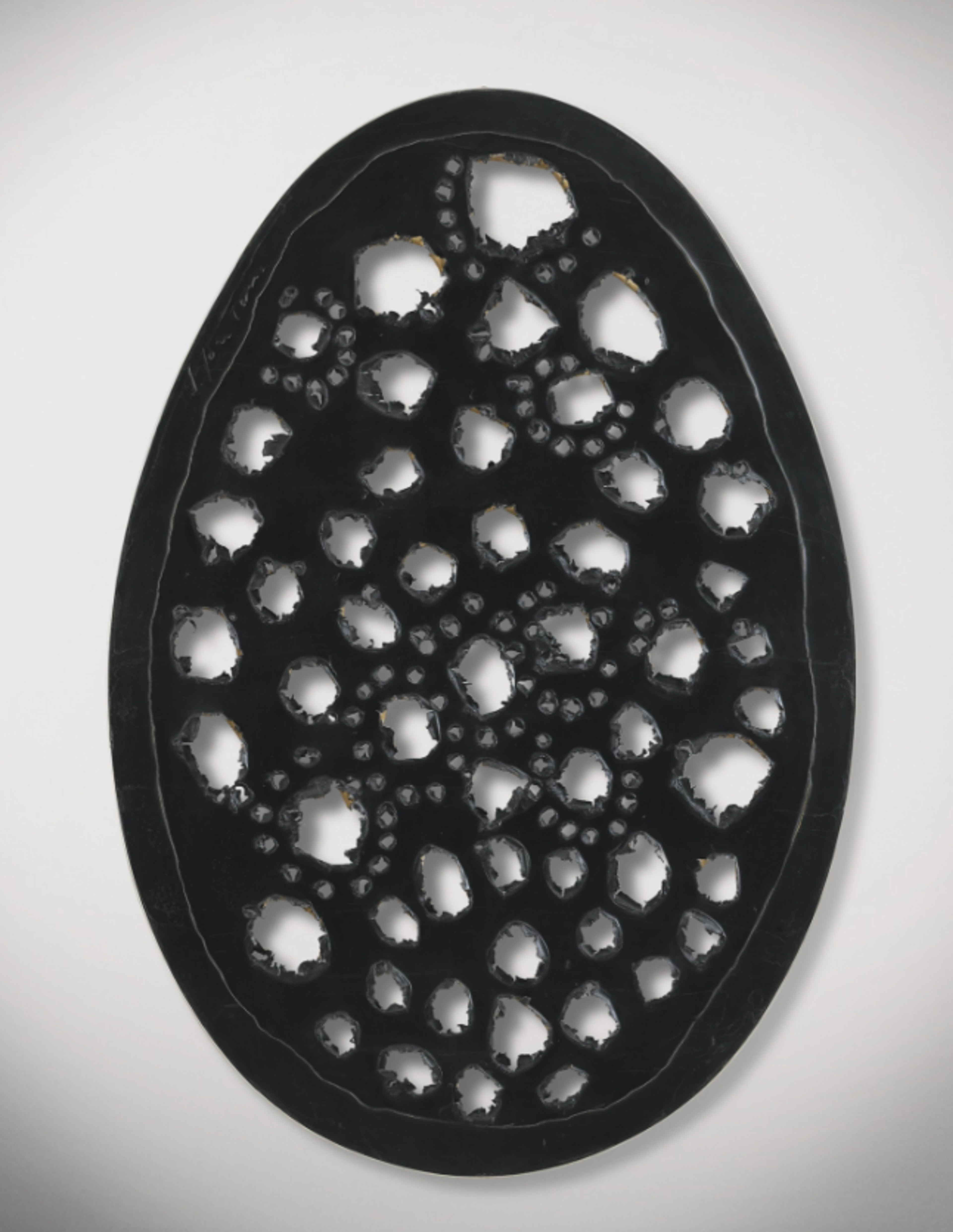 A golden brown egg-shaped canvas decorated with perforations of different sizes. One large perforation in the upper-central section stands out. Other smaller perforations are loosely arranged into lines, curves, and clusters.