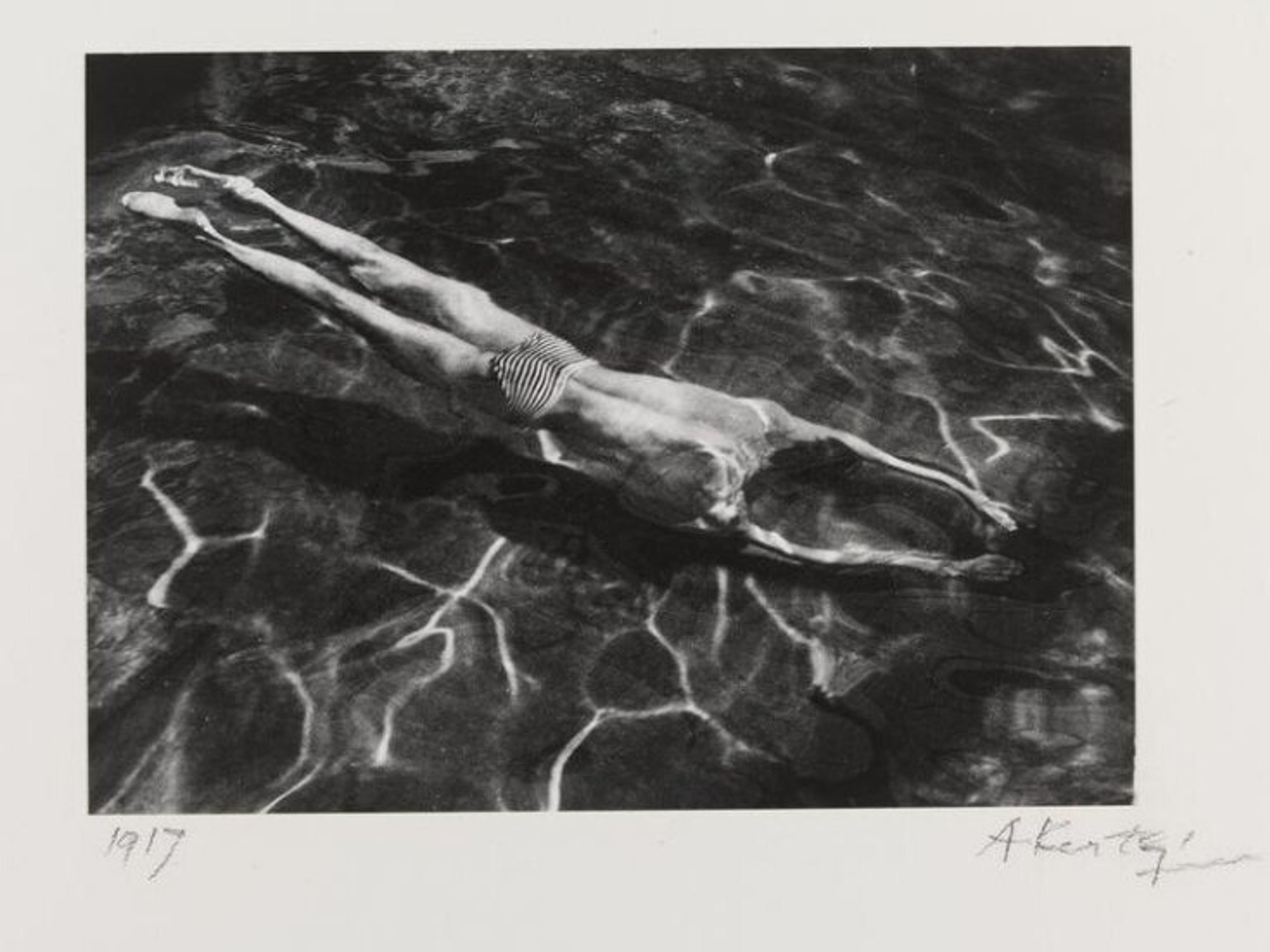 Cette photographie en noir et blanc montre un homme nageant sous l'eau.
