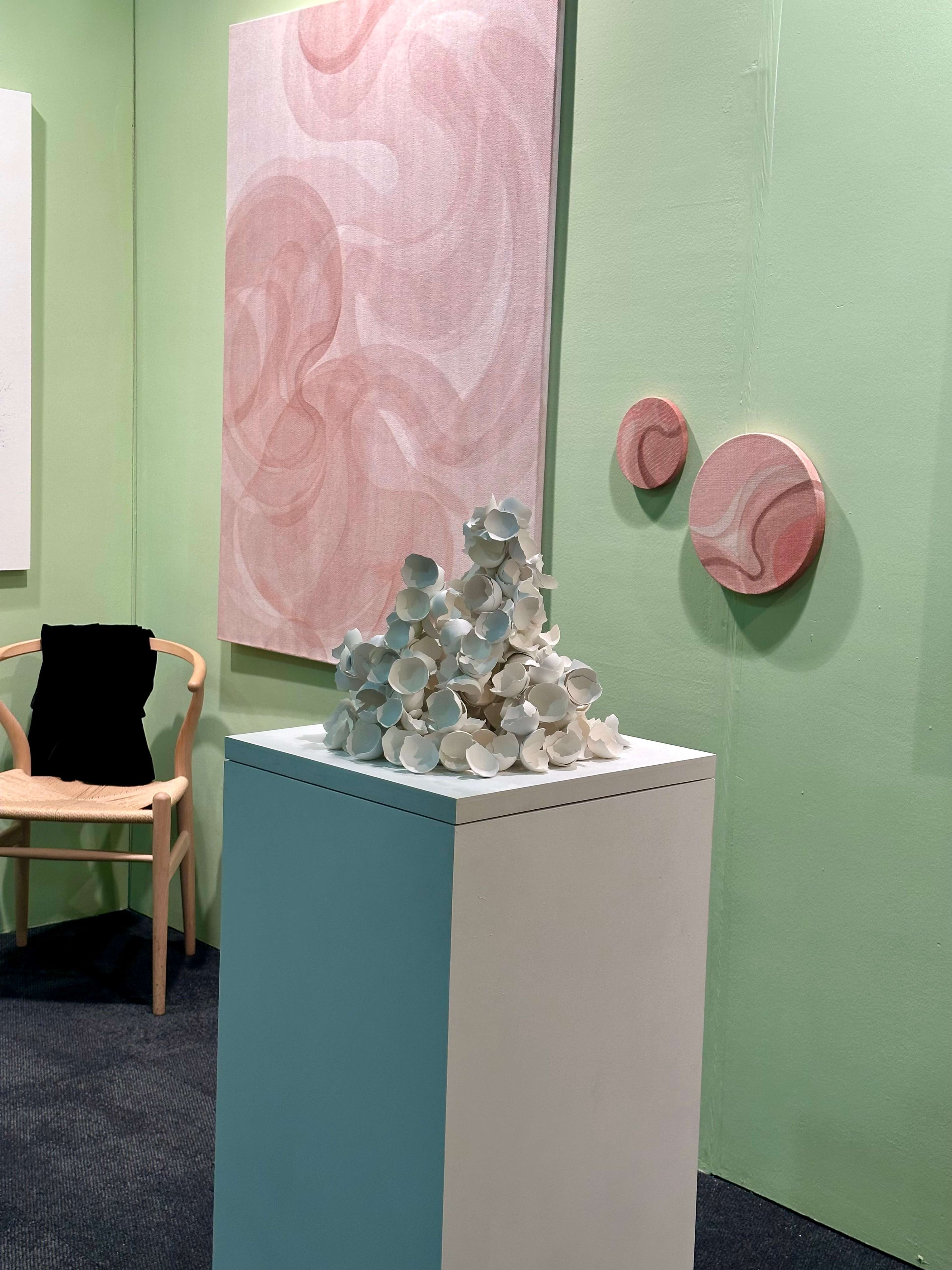 Une pile de coquilles d'œufs brisées repose sur un socle, entourée d'œuvres d'art accrochées.