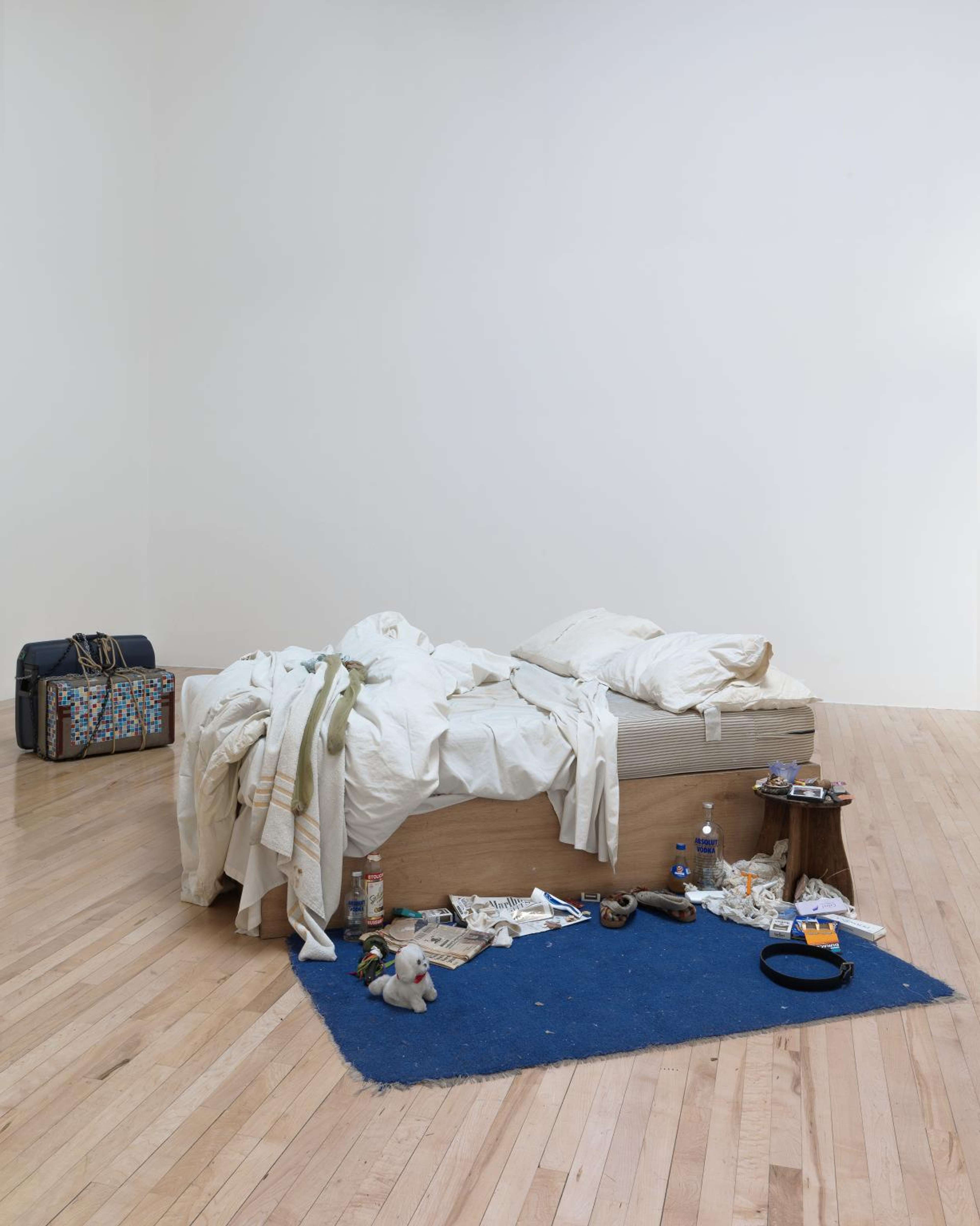 Photographie de *My Bed* (1998), une œuvre en installation de l'artiste Tracey Emin. Elle représente un lit défait, entouré de bouteilles d'alcool vides, de mégots de cigarettes et de préservatifs usagés.