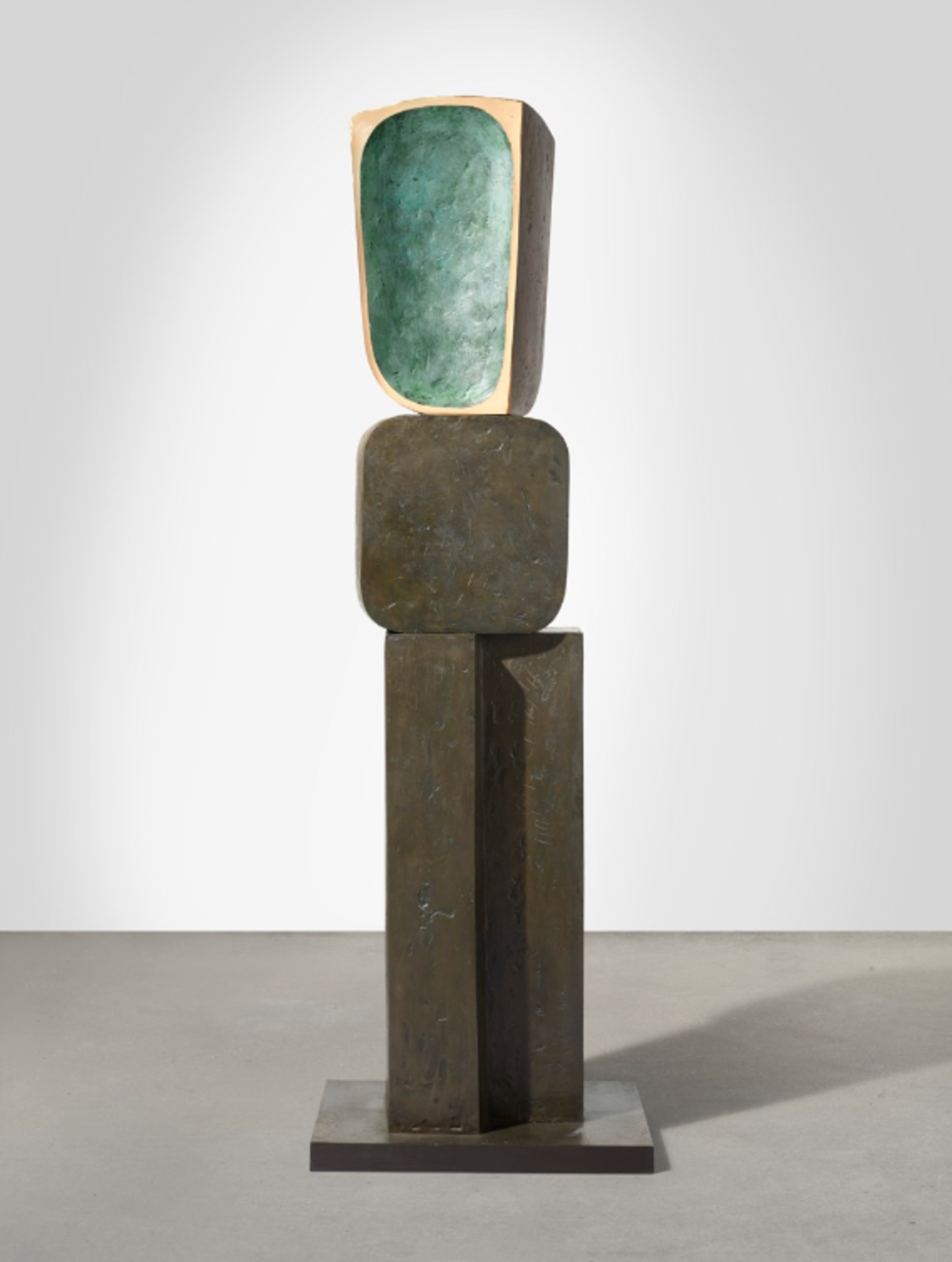 A tall, slender bronze sculpture consisting of three distinct geometric sections stacked vertically. The top features an irregular rectangular form with a green-hued hollow, the middle section is a square element with rounded corners, and the bottom is a ridged vertical column with an L-shaped base. The entire piece has a dark brown patina with green accents visible in the recessed areas.