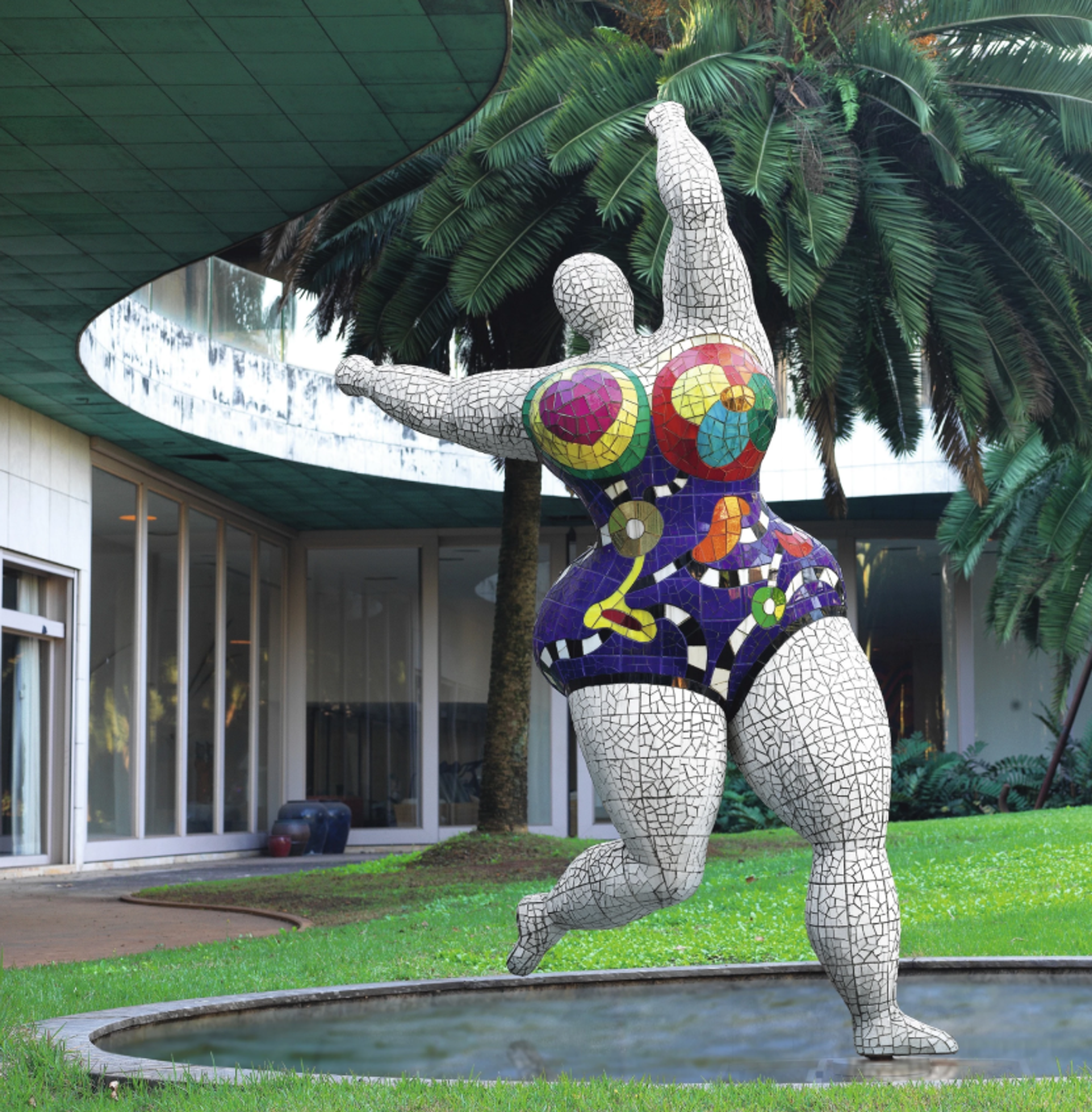 A large-scale mosaic sculpture of a dancing figure with a mosaic white surface texture and colourful patterned swimsuit or leotard. Her pose, with raised back leg and arms thrown to the sky, suggests joy and celebration.