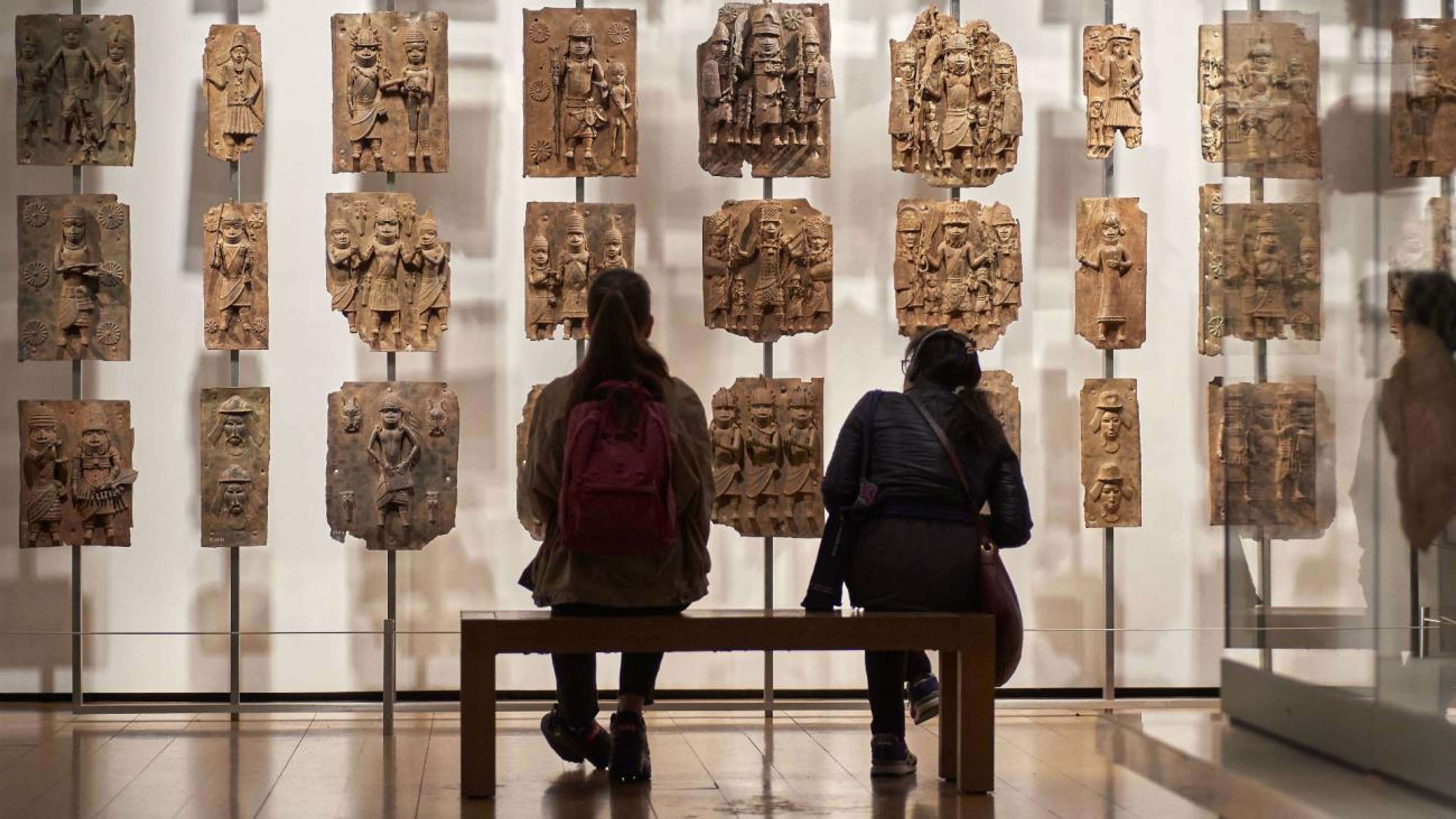 Une photo de deux visiteurs assis devant les bronzes du Bénin exposés au British Museum.
