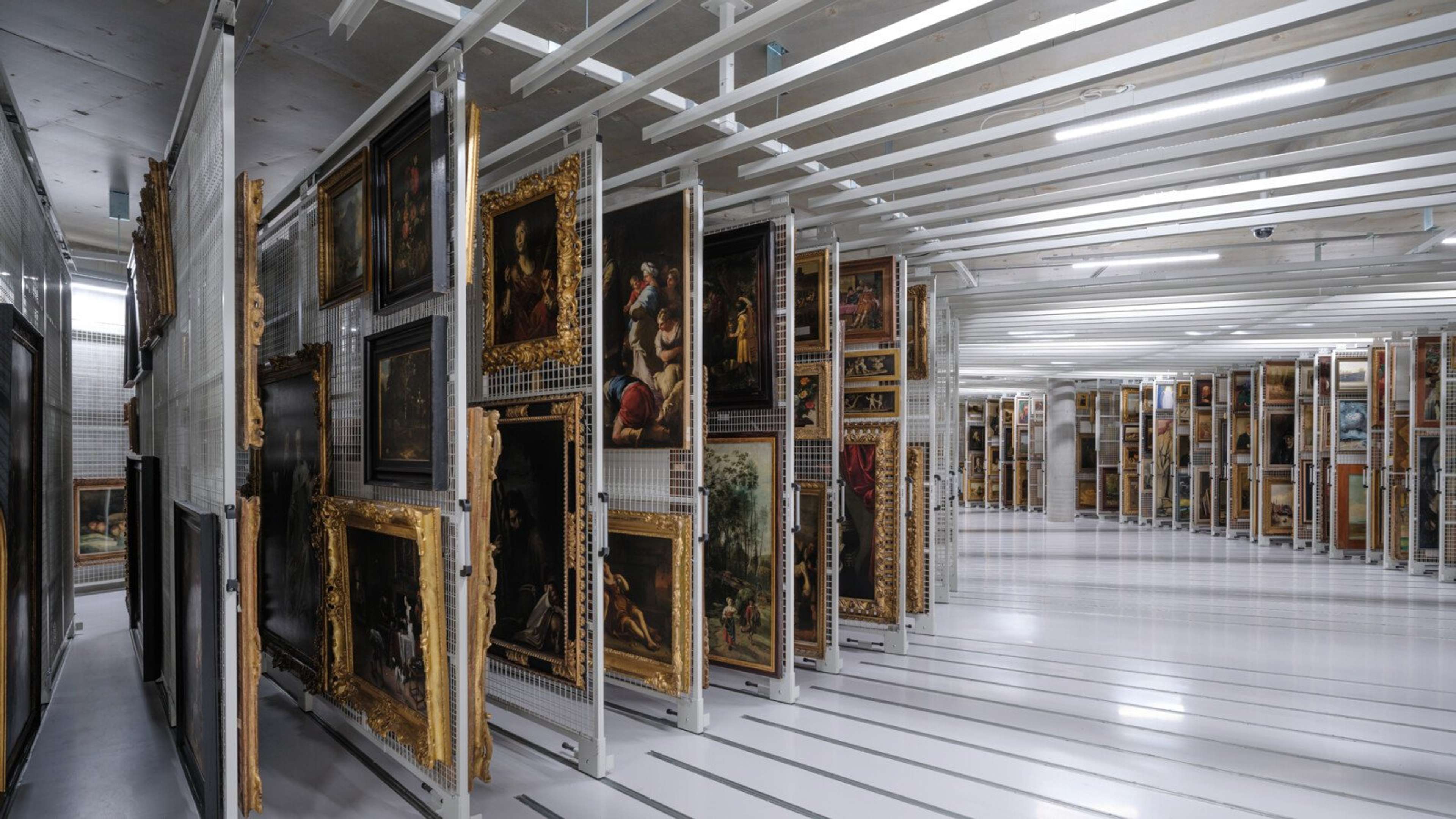 Des tableaux dans des cadres dorés, stockés dans un système de rangement d'archives incurvé