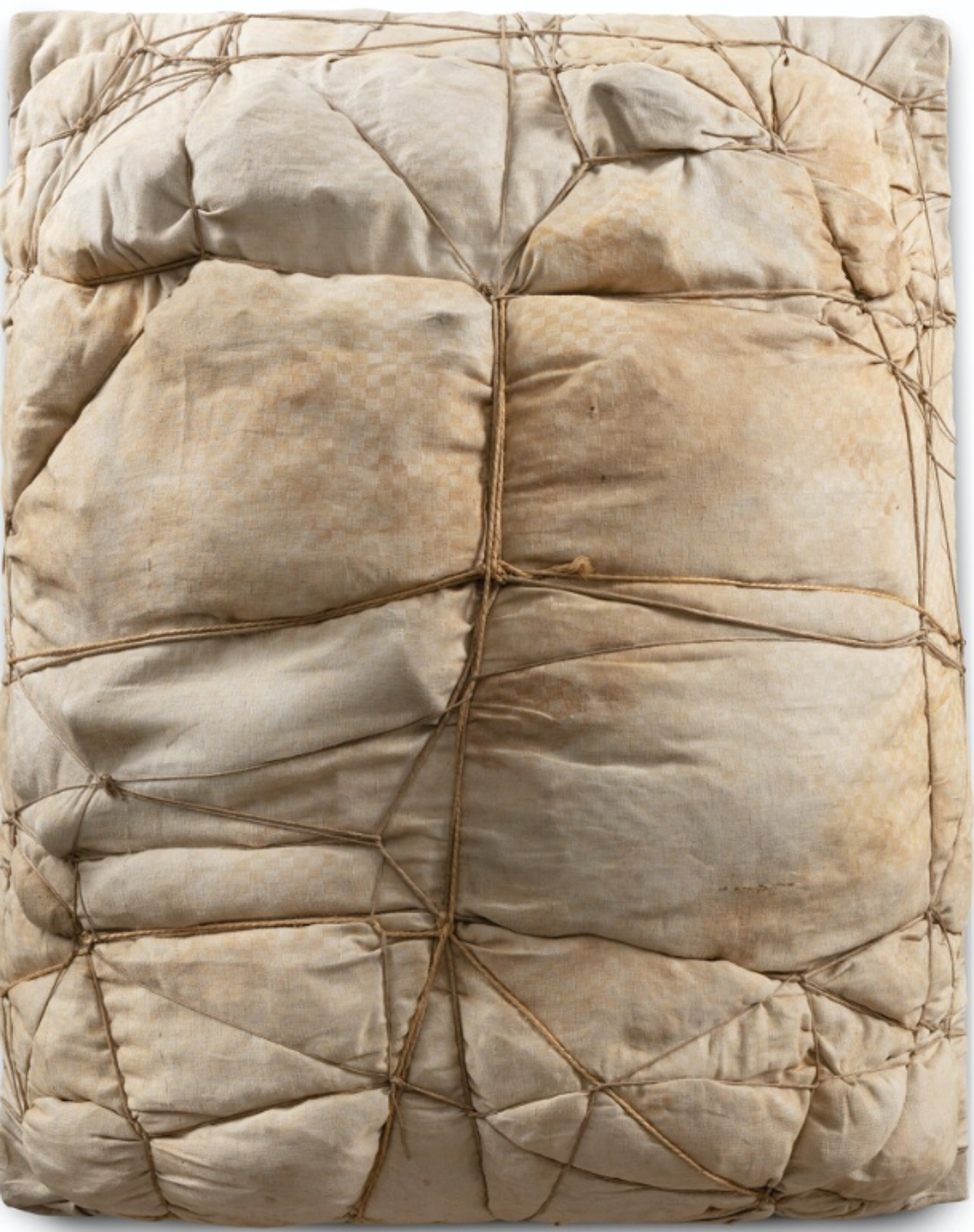 A sculptural artwork showing a package wrapped in white or cream-coloured fabric and tied with rope, creating a pattern of bulging, cushioned sections across its surface. The contents are unidentifiable. The fabric is pulled taut in some areas and bunched in others.
