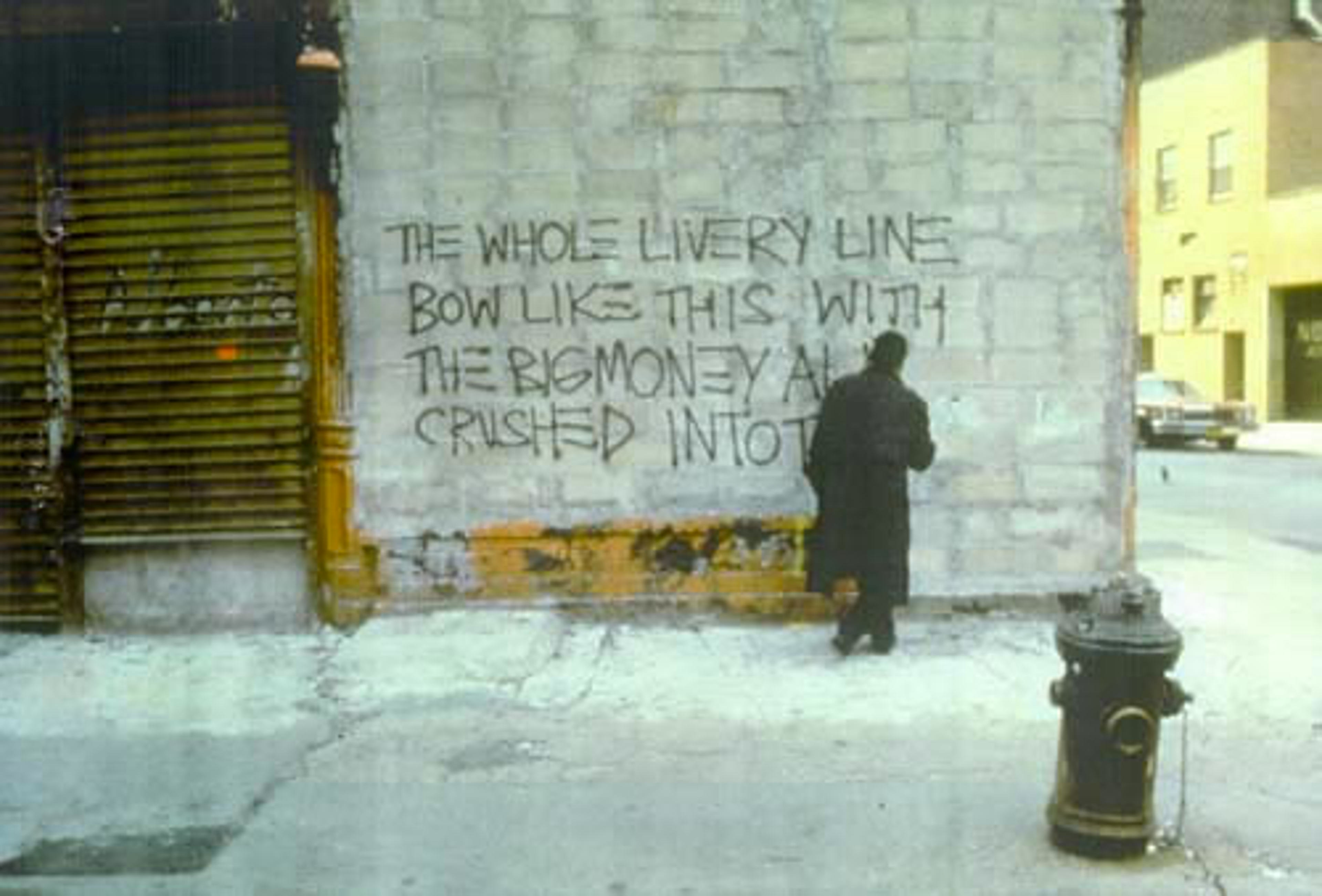Cette photographie montre Basquiat peignant au spray sur un mur les lignes suivantes : « the whole livery line bow like this with the big money all crushed into these feet »