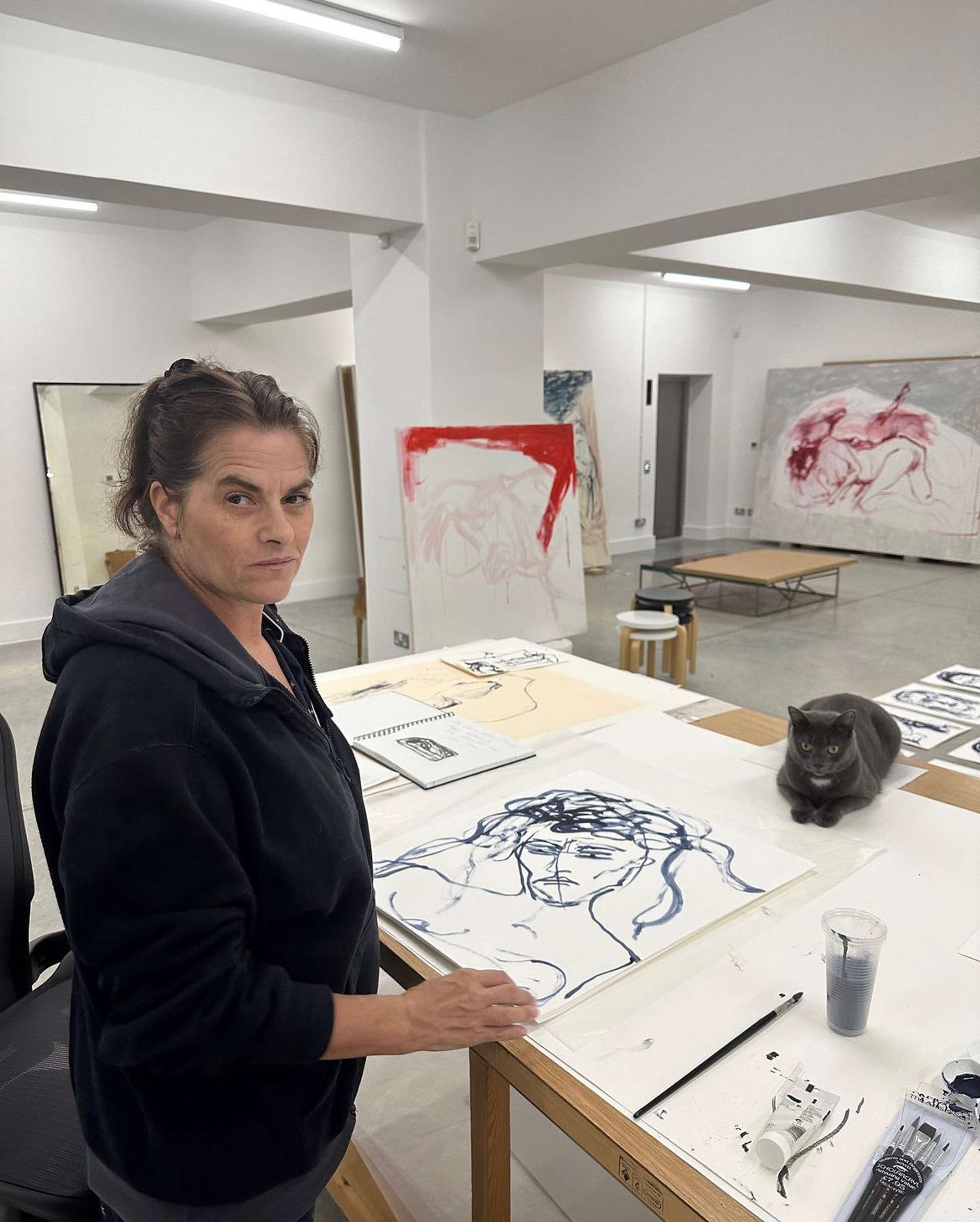 Une image de l'artiste Tracey Emin dans son atelier, dessinant les œuvres qui ont été gravées sur les portes en bronze. L'artiste regarde l'objectif tandis qu'un chat est allongé à l'arrière-plan.