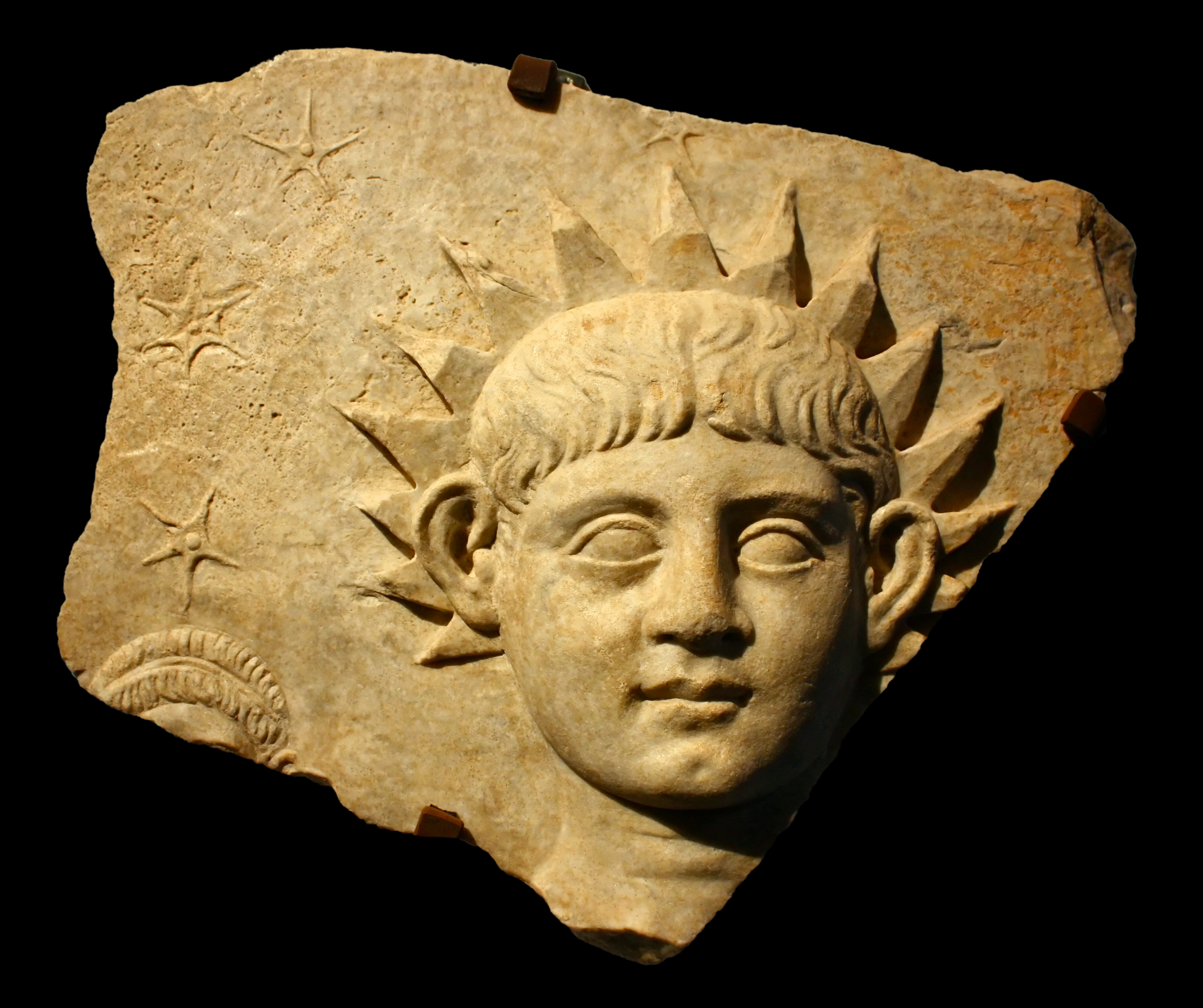 Sculpture romaine antique représentant un jeune garçon dont les cheveux rayonnent de lumière solaire.