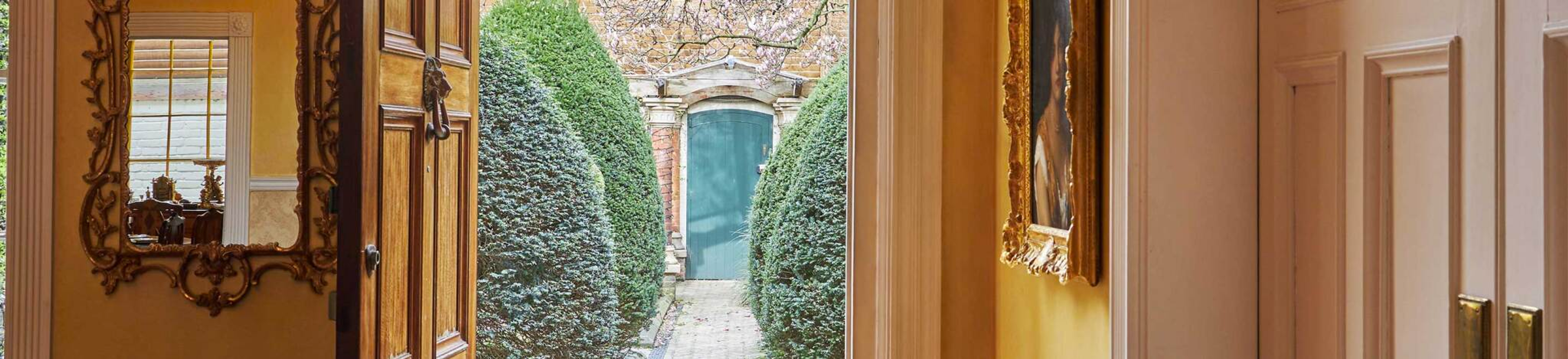 Une image de Garden Lodge, la maison de Freddie Mercury. Elle montre un miroir doré à gauche et un tableau à droite. Au centre, un passage mène au jardin et à la porte d'entrée.