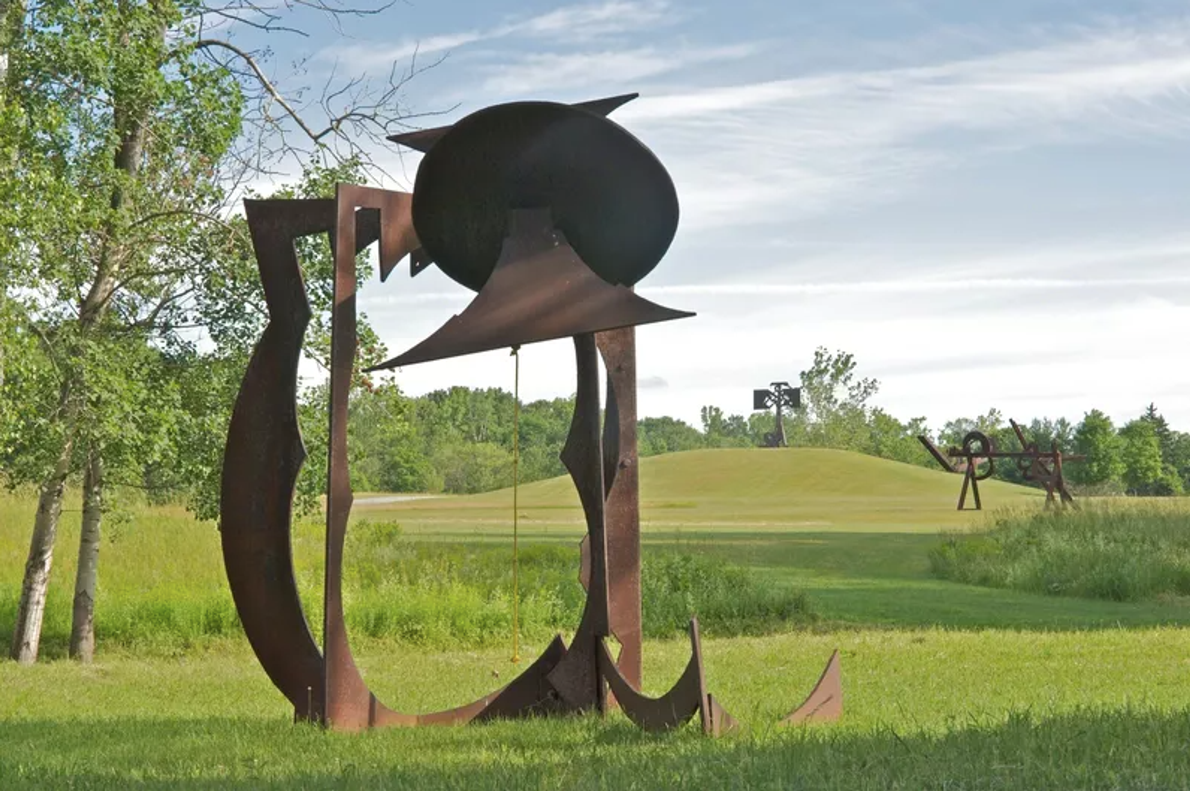 Une sculpture extérieure en acier intitulée « For Chris », créée par Mark di Suvero en 1991. Cette œuvre se compose de plusieurs poutres en acier, larges et courbes, peintes d'un rouge vif, qui s'entrecroisent pour former une structure dynamique.