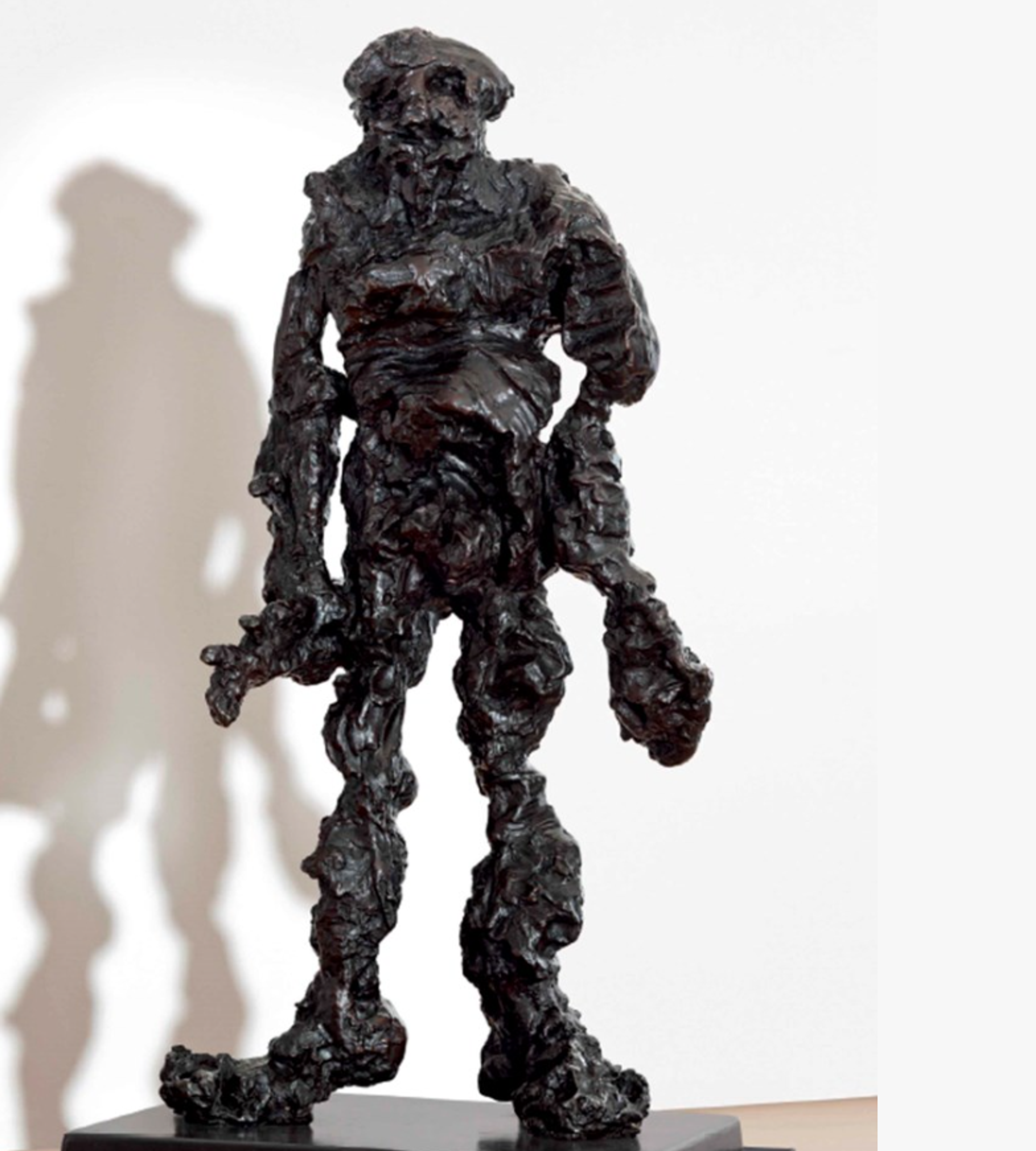 A black, textured sculpture of a standing human figure with an irregular, rough surface. The figure appears abstract with a somewhat bulky form and stands on a small base.