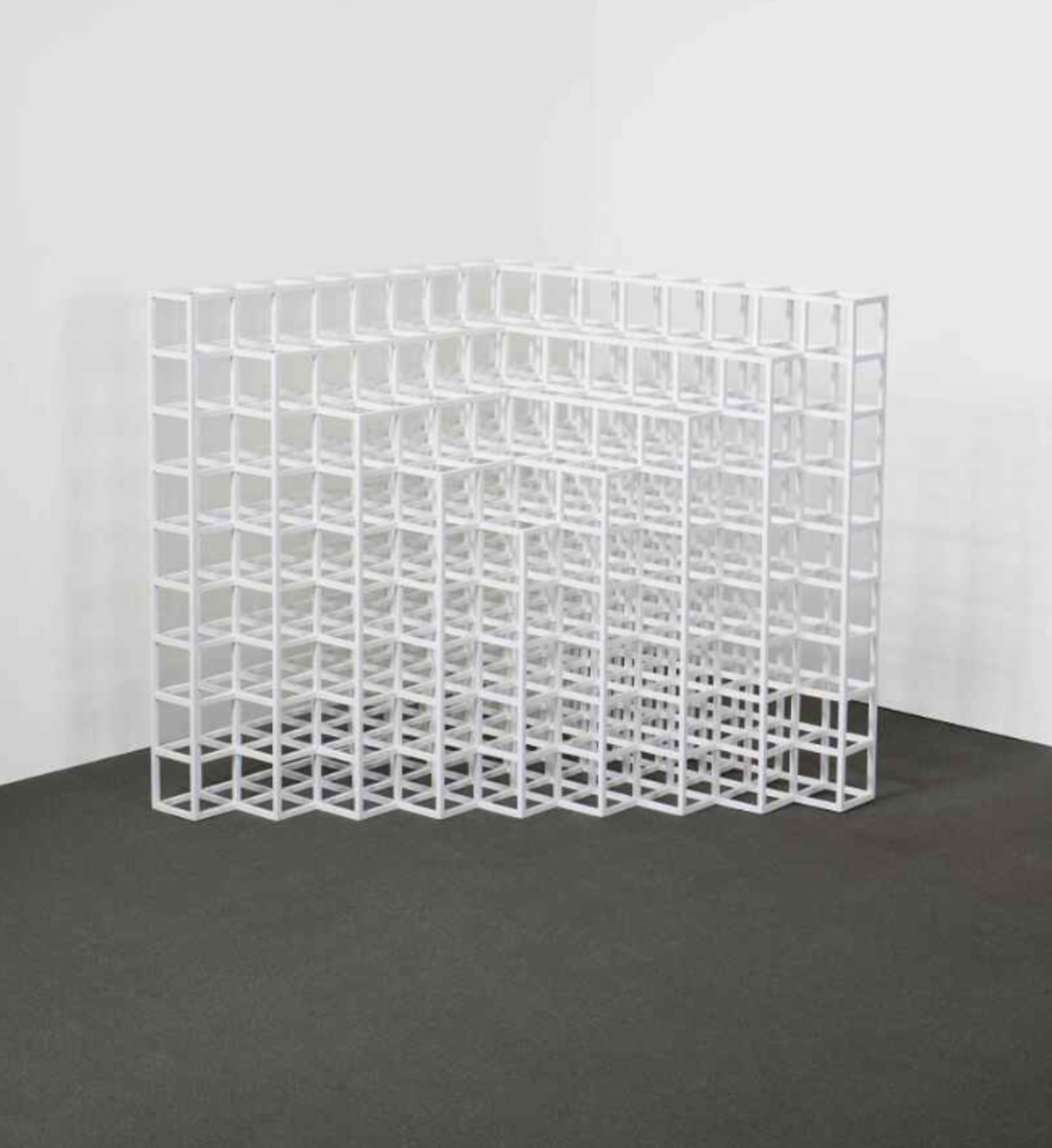 A geometric arrangement of open white cubes designed to fit perfectly into the corner of a room. The structure has the effect of blocking off the corner, with each plane of cubes getting shorter towards the front.
