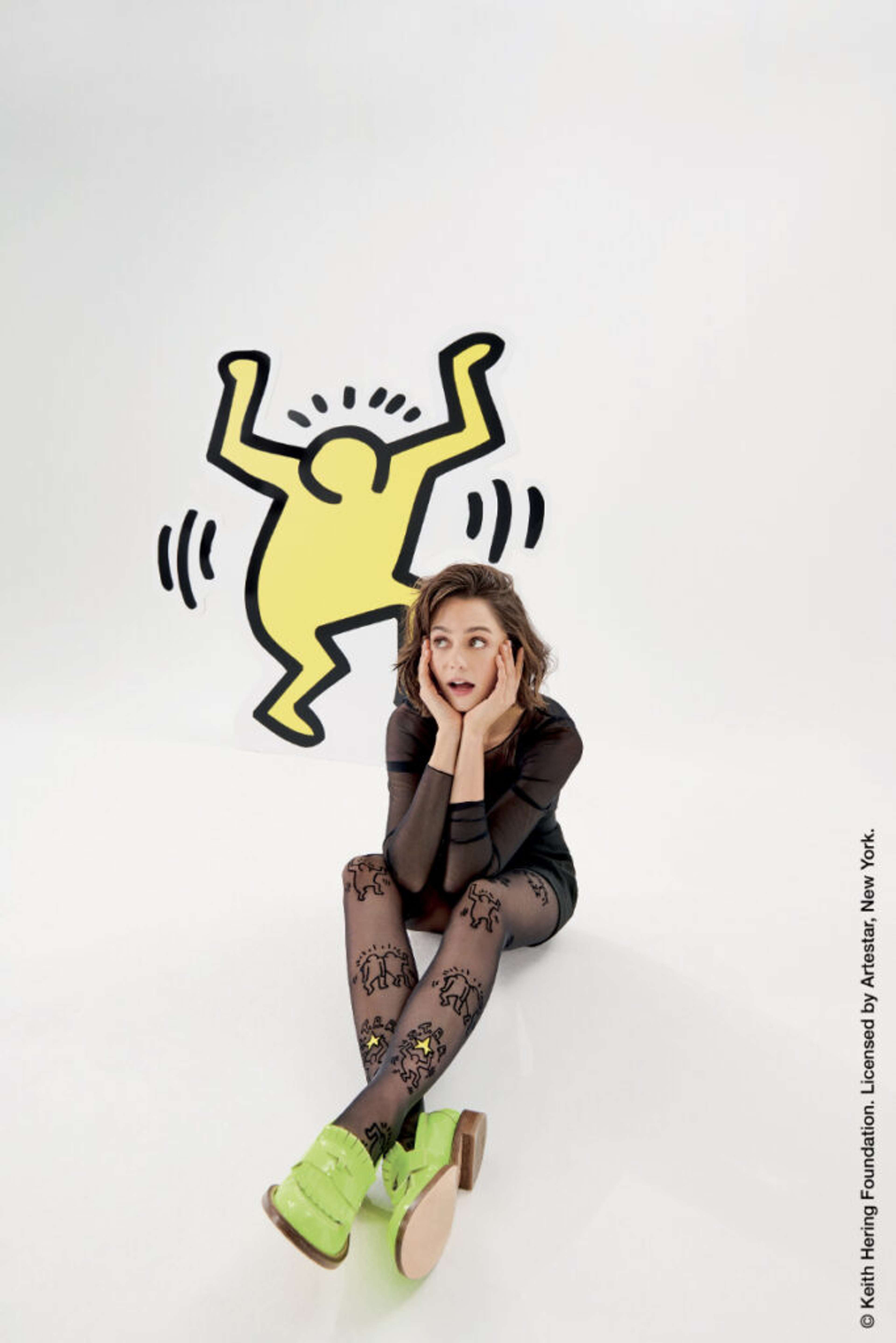 Une photo d'un mannequin portant des collants Calzedonia ornés de motifs de Keith Haring, se tenant devant un arrière-plan décoré d'une des silhouettes emblématiques de l'artiste.