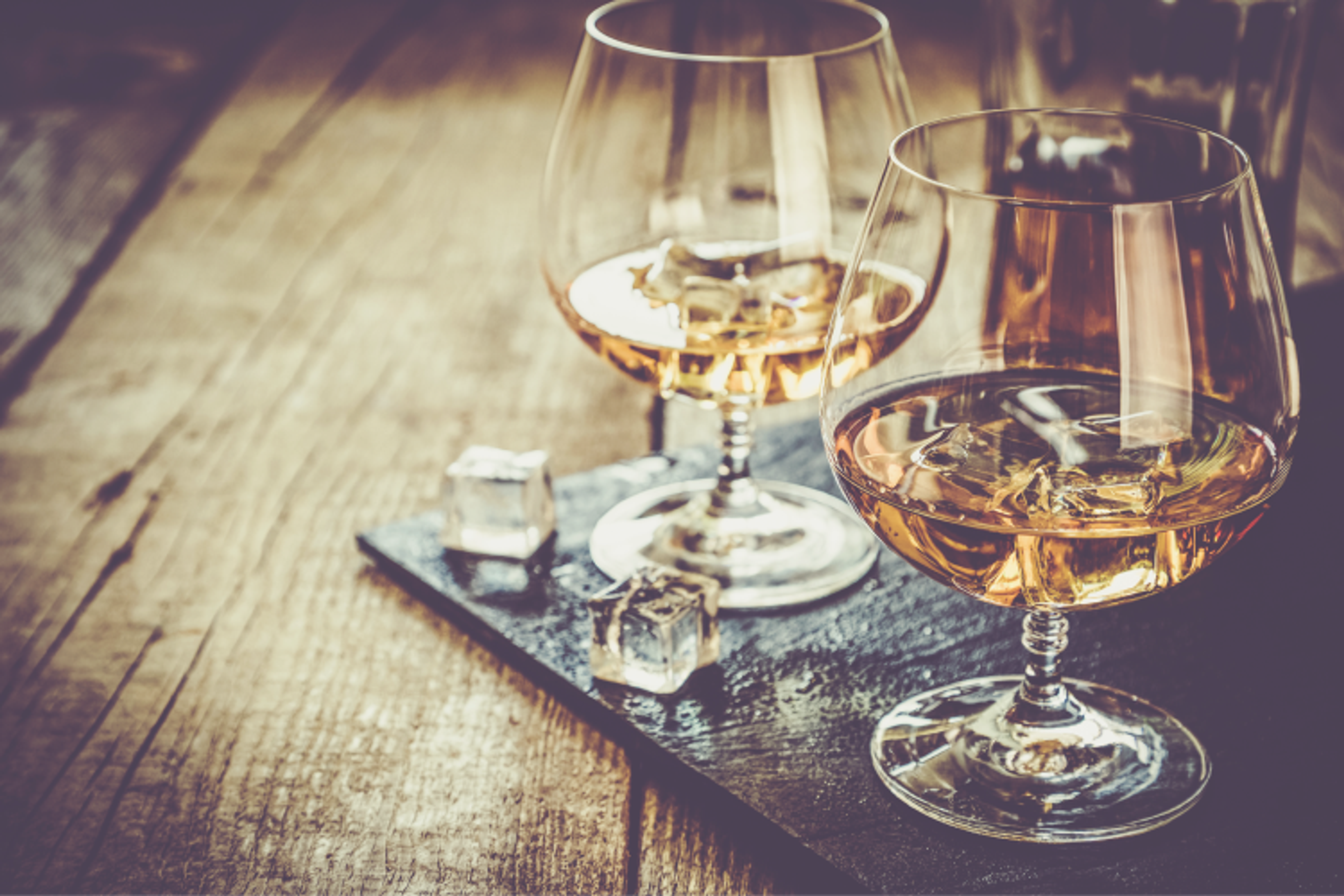 Une image de deux verres de whisky sur glace, posés sur une table en bois.