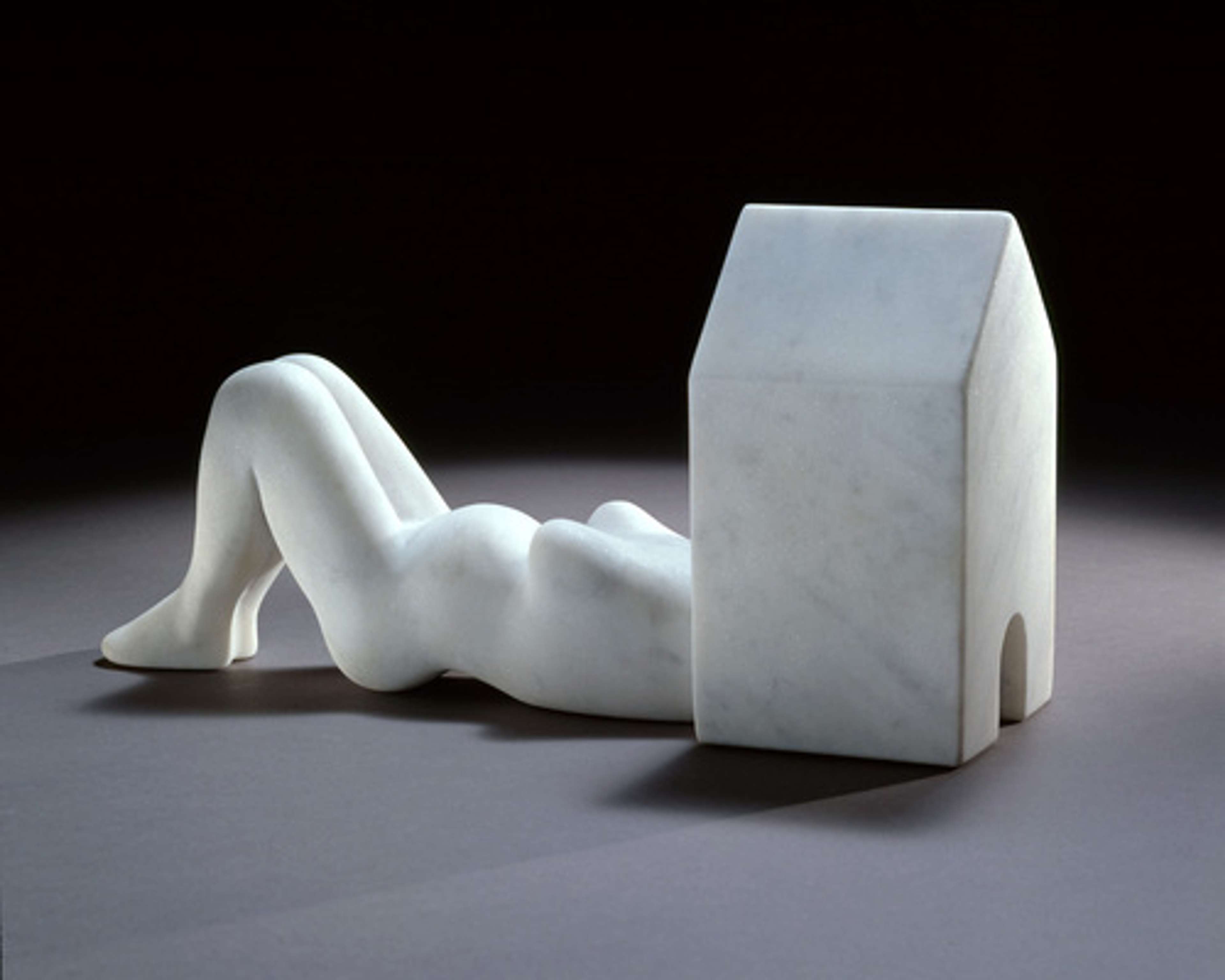 Sculpture en marbre blanc représentant une femme enceinte allongée, la tête à l'intérieur d'une structure domestique. L'œuvre s'intitule « At Home ».