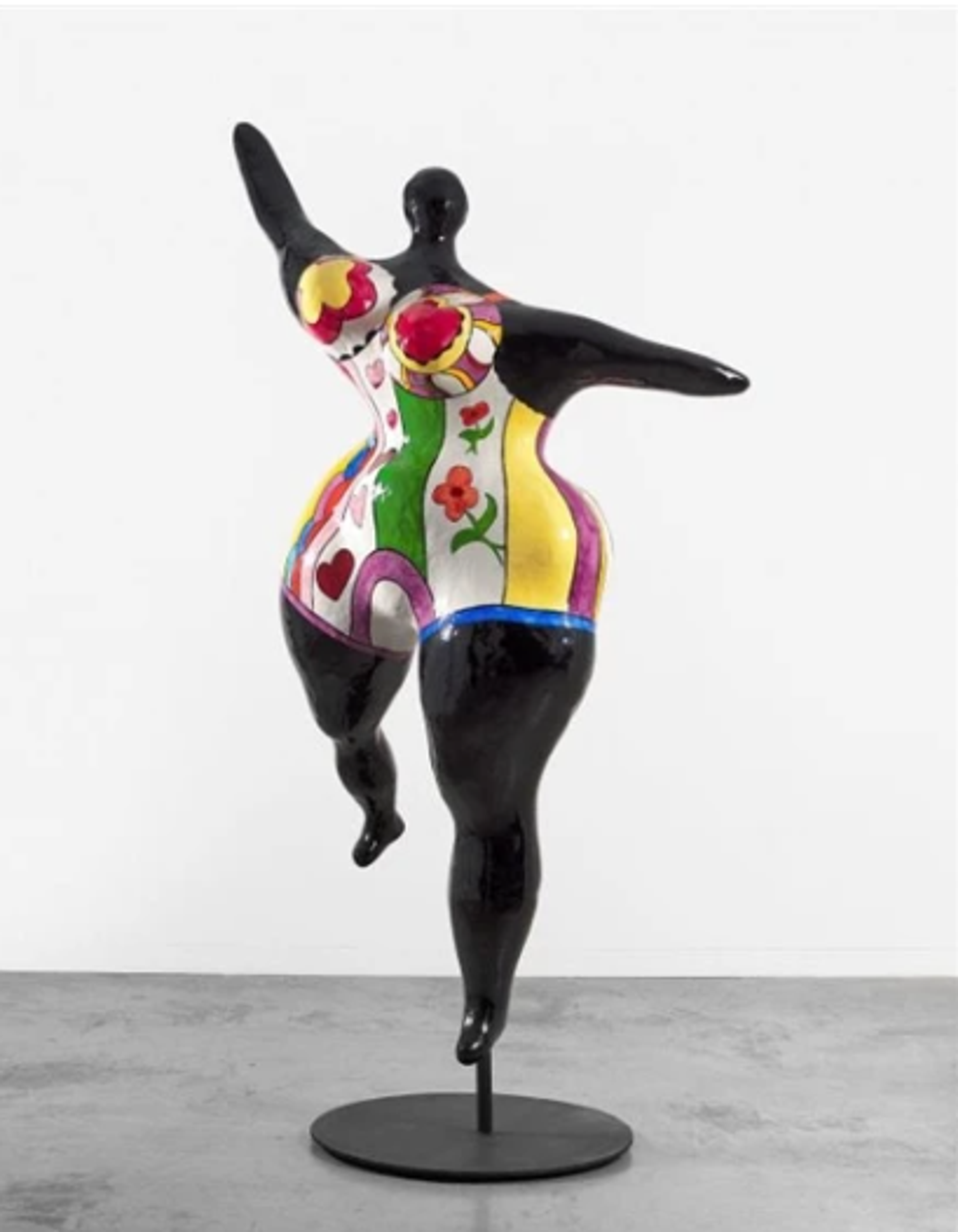A dynamic black sculptural figure in mid-dance, balanced gracefully on one leg. The torso features vibrant patterns in multiple colours, creating a striking contrast with the black limbs.