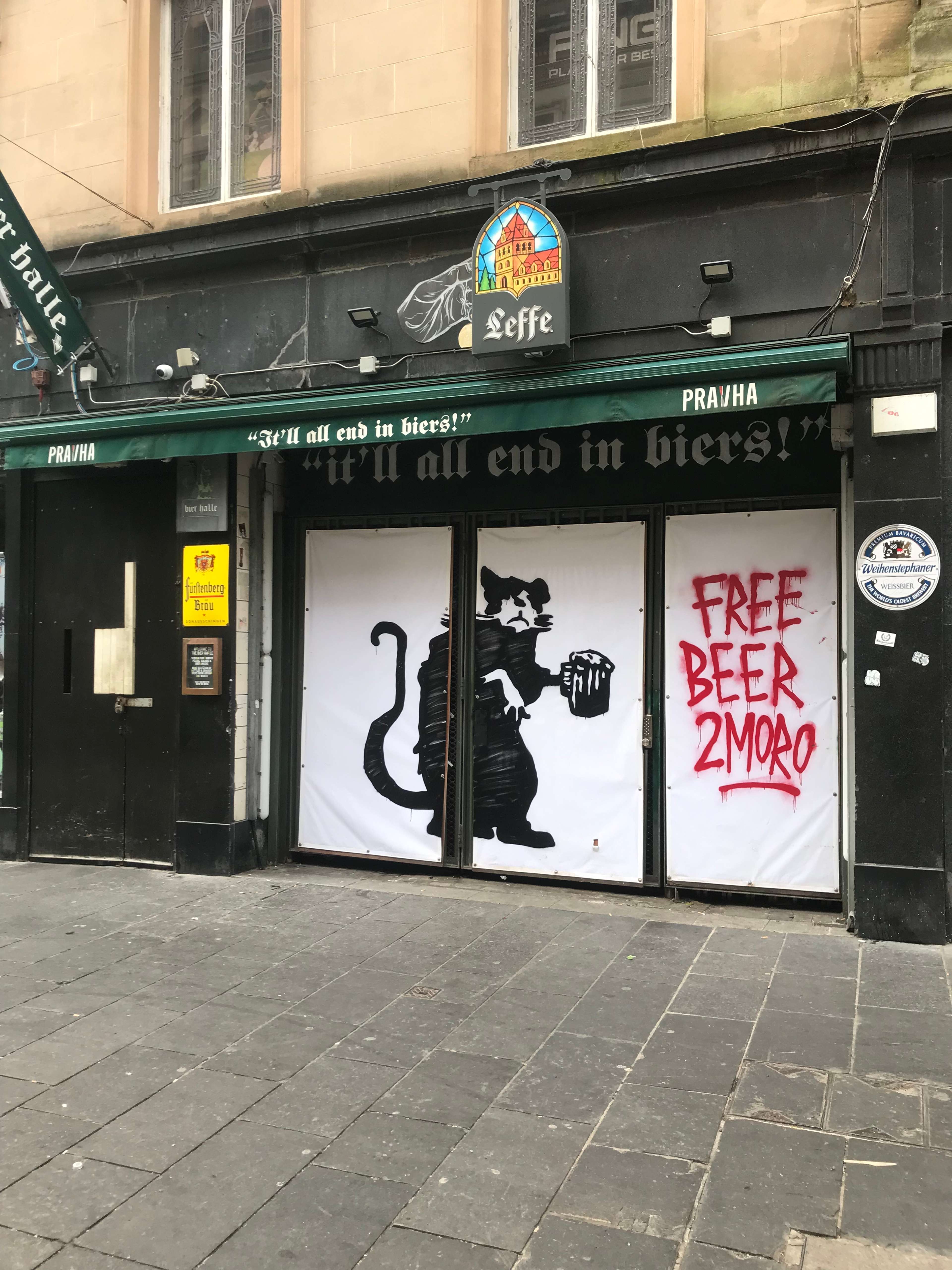 Une œuvre de street art représentant un rat tenant une pinte de bière, avec les mots « FREE BEER 2MORO » peints en rouge à côté sur la façade d’un pub.