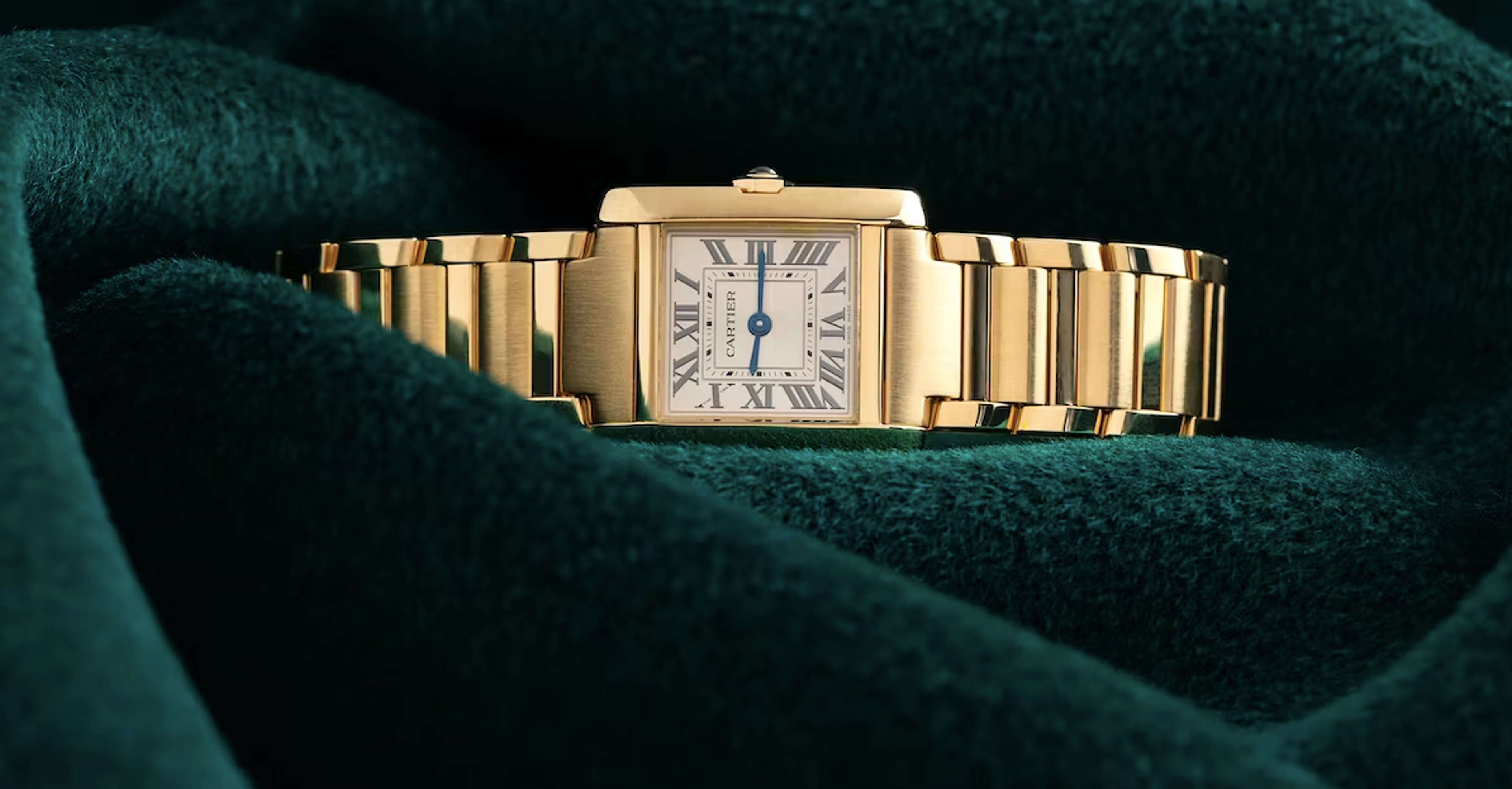 Une Cartier Tank Française en or est posée sur un tissu en velours vert ; ce modèle a été lancé pour la première fois en 1917.